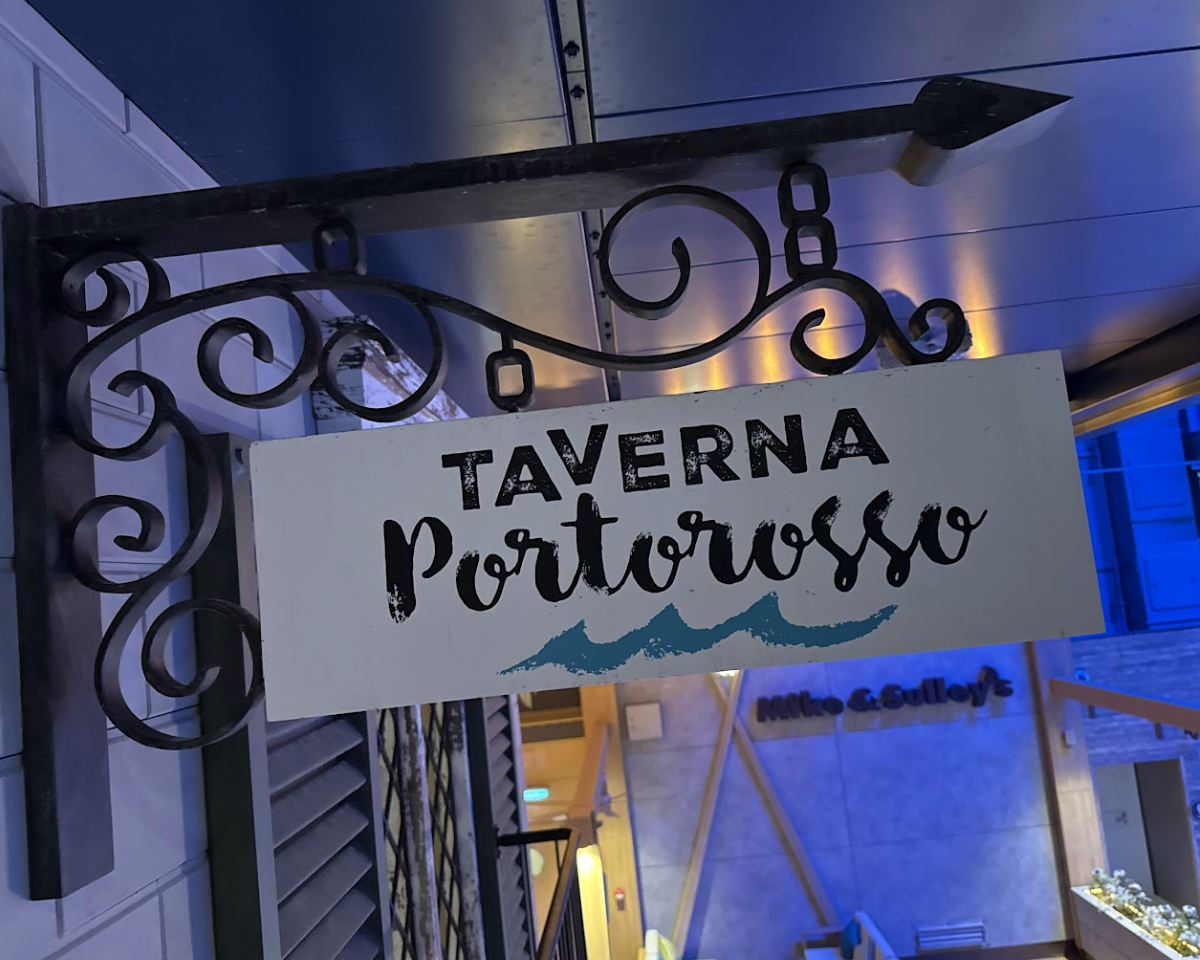 The wrought-iron black signpost holds the white Taverna Portorosso sign. A simplistic blue wave image sits beneath the black text.
