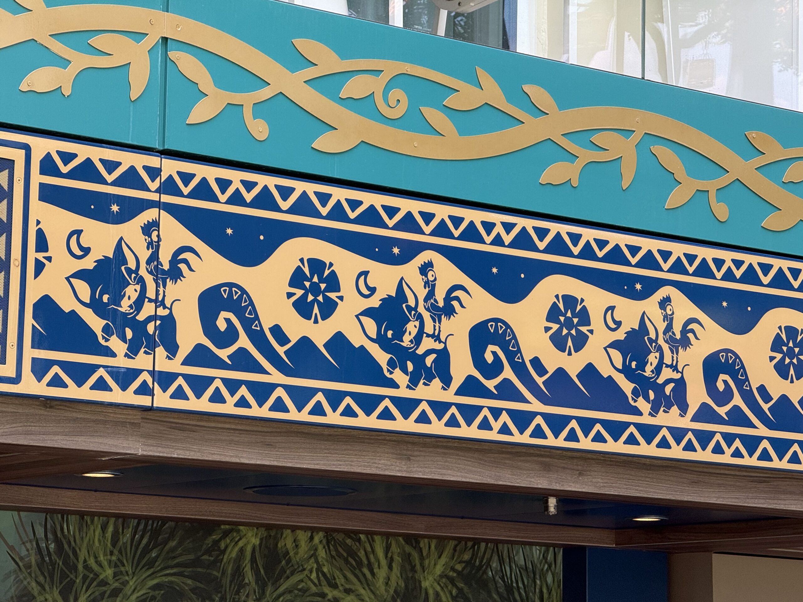 There are some tables "outside" with more mural scenes and flowers surrounding the space. Along the top are two runners—one is teal with gold design elements, which blend in with the rest of Imagination Garden, and the other is a dark navy with tan tribal designs surrounding the images of Hei Hei and Pua.