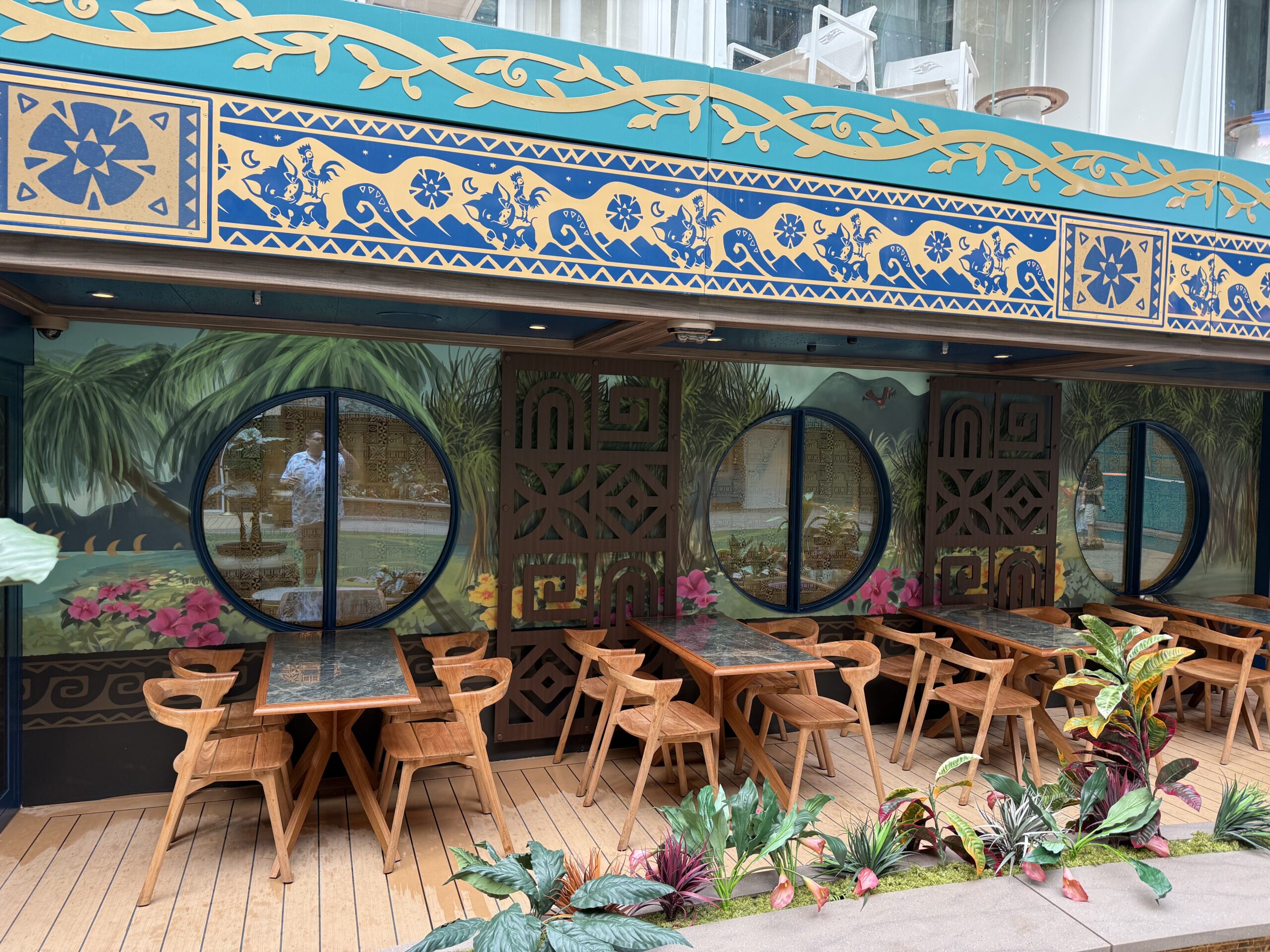 There are some tables "outside" with more mural scenes and flowers surrounding the space. Along the top are two runners—one is teal with gold design elements, which blend in with the rest of Imagination Garden, and the other is a dark navy with tan tribal designs surrounding the images of Hei Hei and Pua.