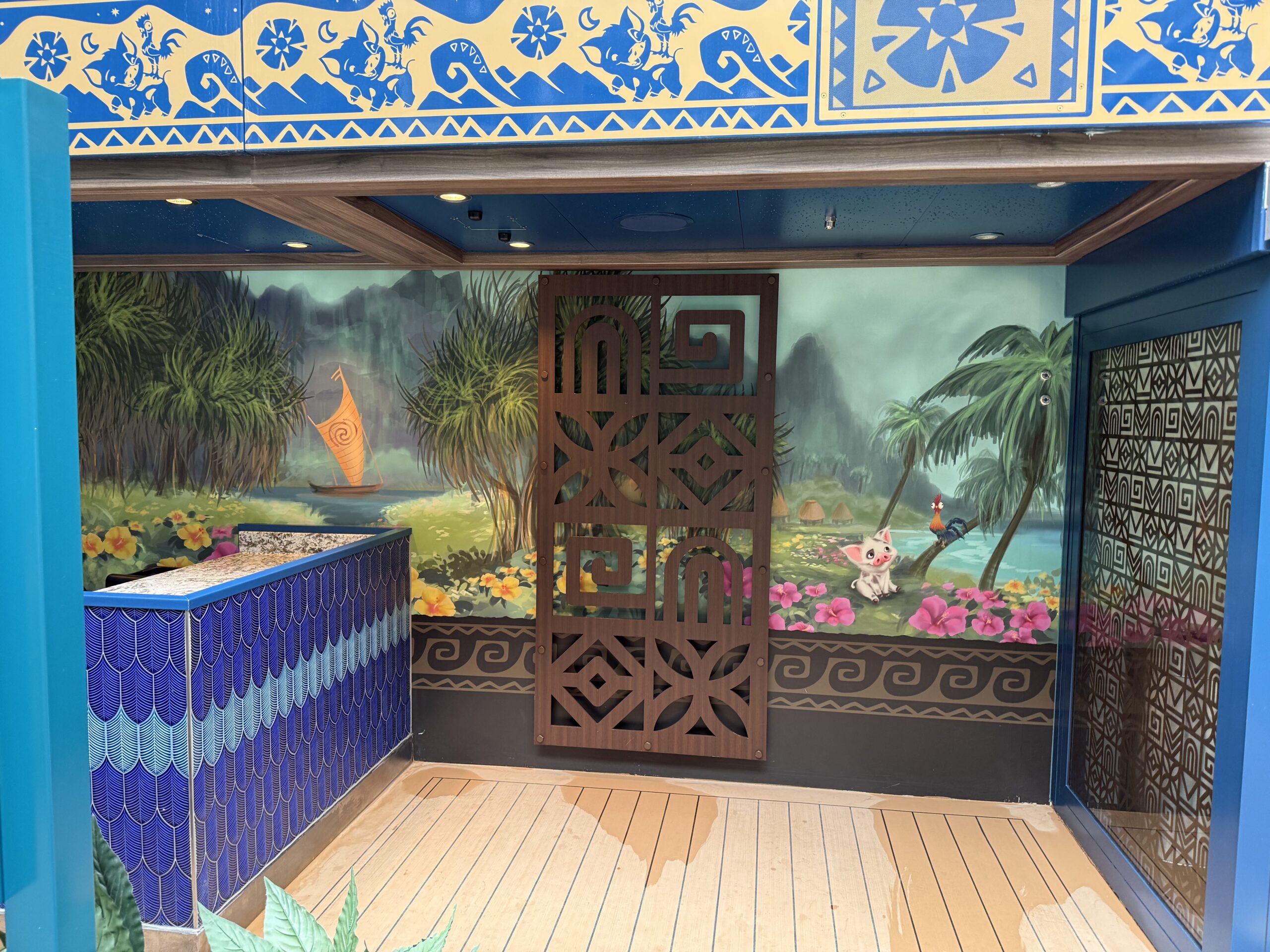 On either side of the entrance, a Moana-themed mural shows Hei Hei and Pua standing in a lush garden near the ocean. Palm trees float in the window while mountains tower in the back.