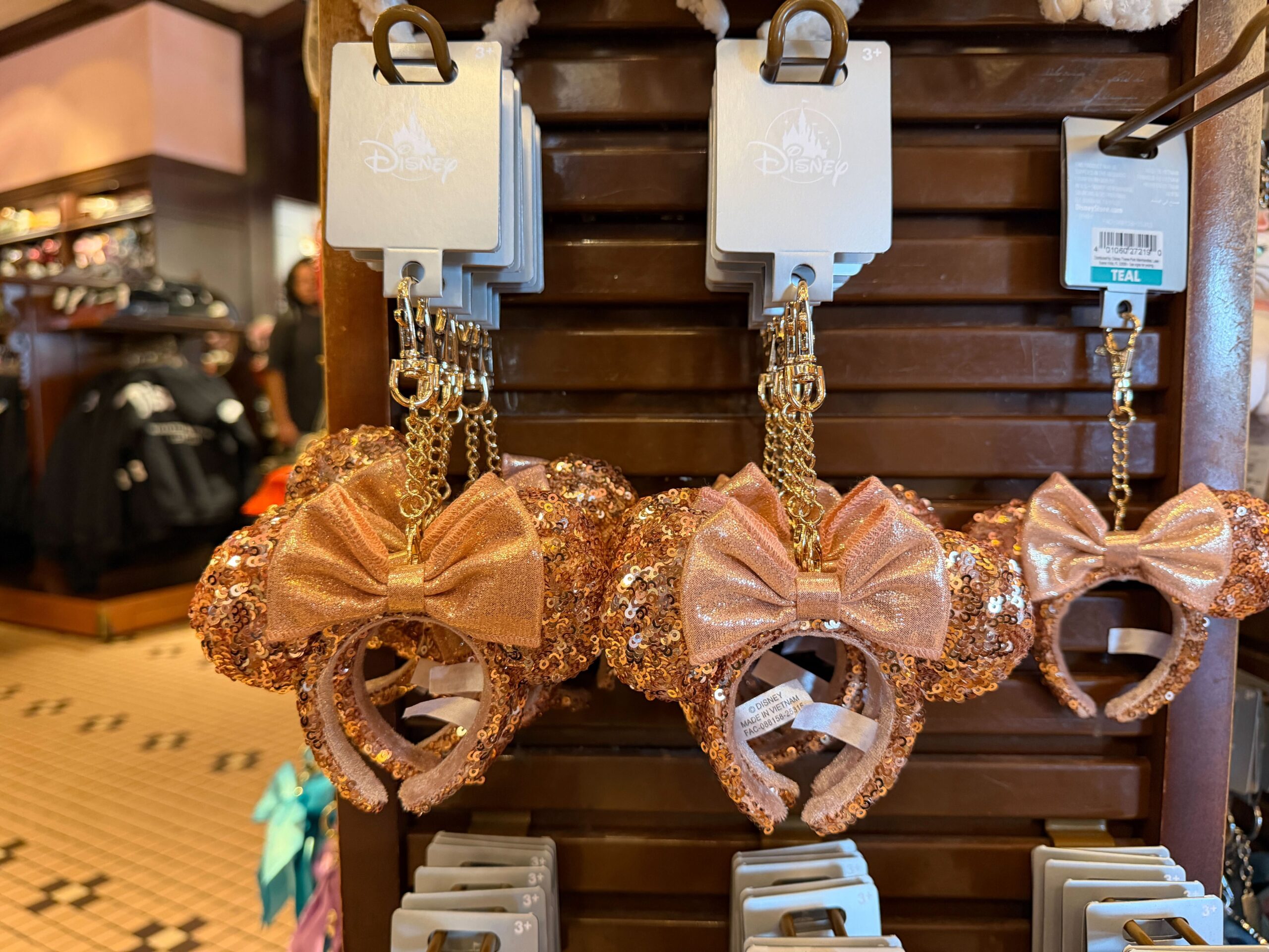 Another ear headband keychain is covered in rose gold sequins with a shimmering Minnie bow. It hangs on a gold-tone chain.