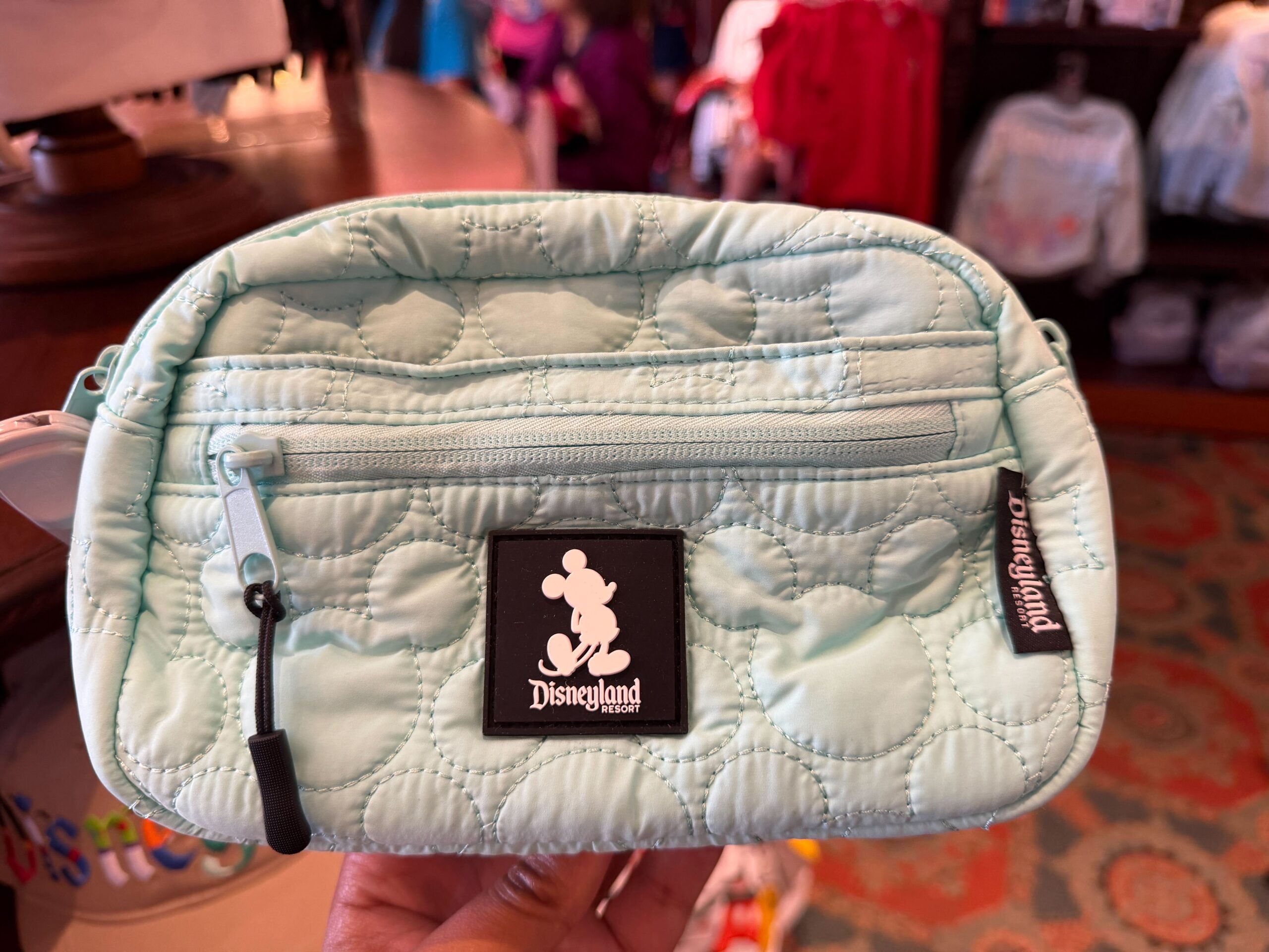 Carry your ear headband and ear headband keychain with one of these holder bags. This belt bag is light blue with an all-over stitched Mickey pattern. A black label on the front features Mickey's silhouette and the Disneyland Resort wordmark.