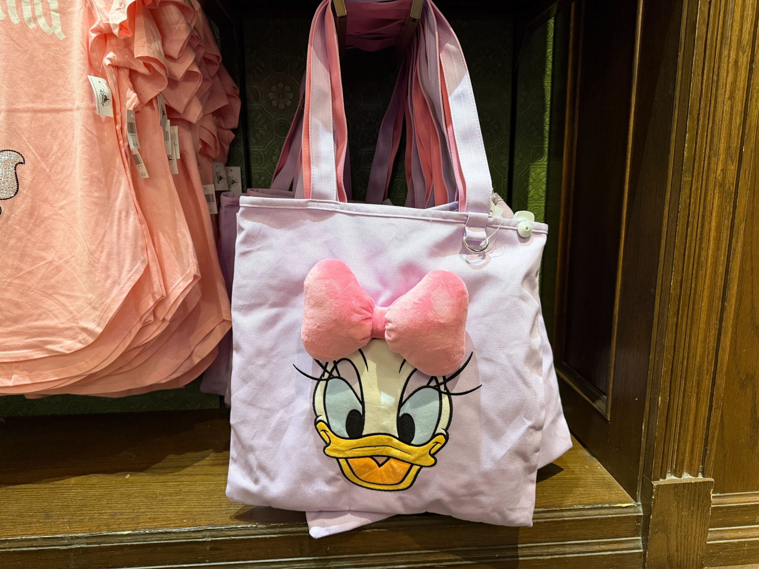 It may not be designed for carrying ears, but you could easily slip a pair into this Daisy Duck tote. It's a light purple square with a pair of pink-lined shoulder straps.