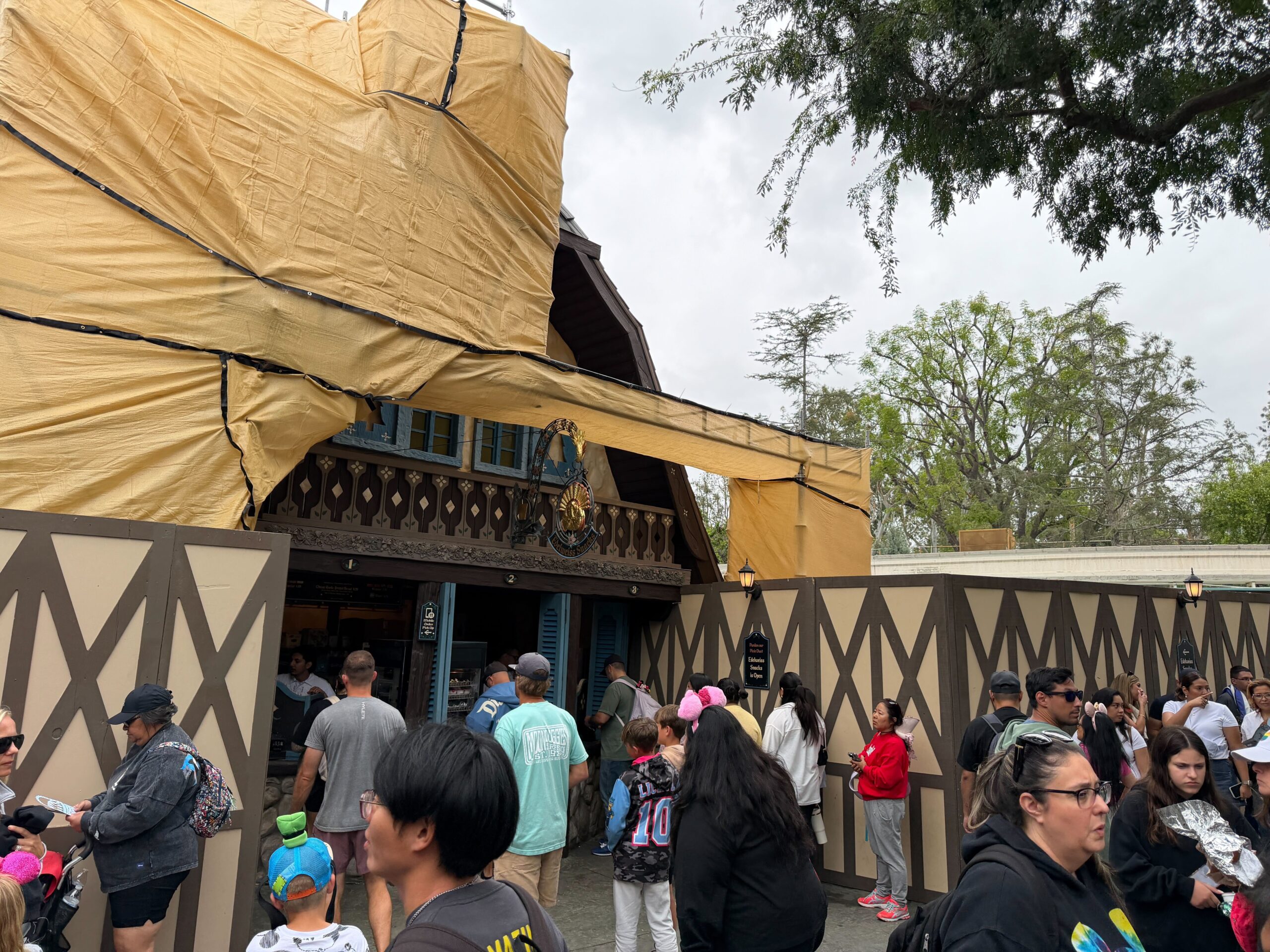 The scaffolding and beige scrim is on the left side and front of Edelweiss Snacks. Construction walls keep guests away from the scaffolding, although it extends over guests heads. The kiosk is still open.