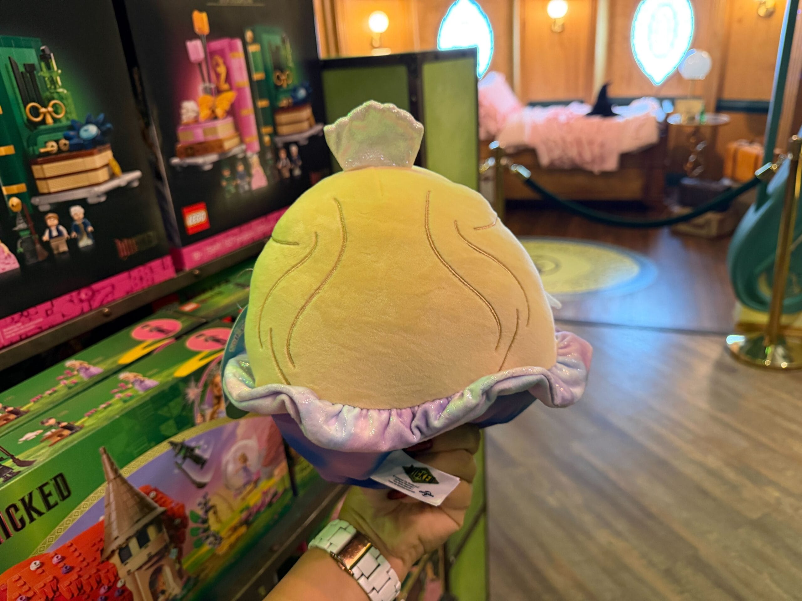 Facial details are also embroidered on the Glinda Squishmallow. She is wearing a little silver tiara, and her purple dress is embroidered with darker purple, pink, and blue details. The skirt of the dress appears to be almost like tie-dye in purple and blue tones.