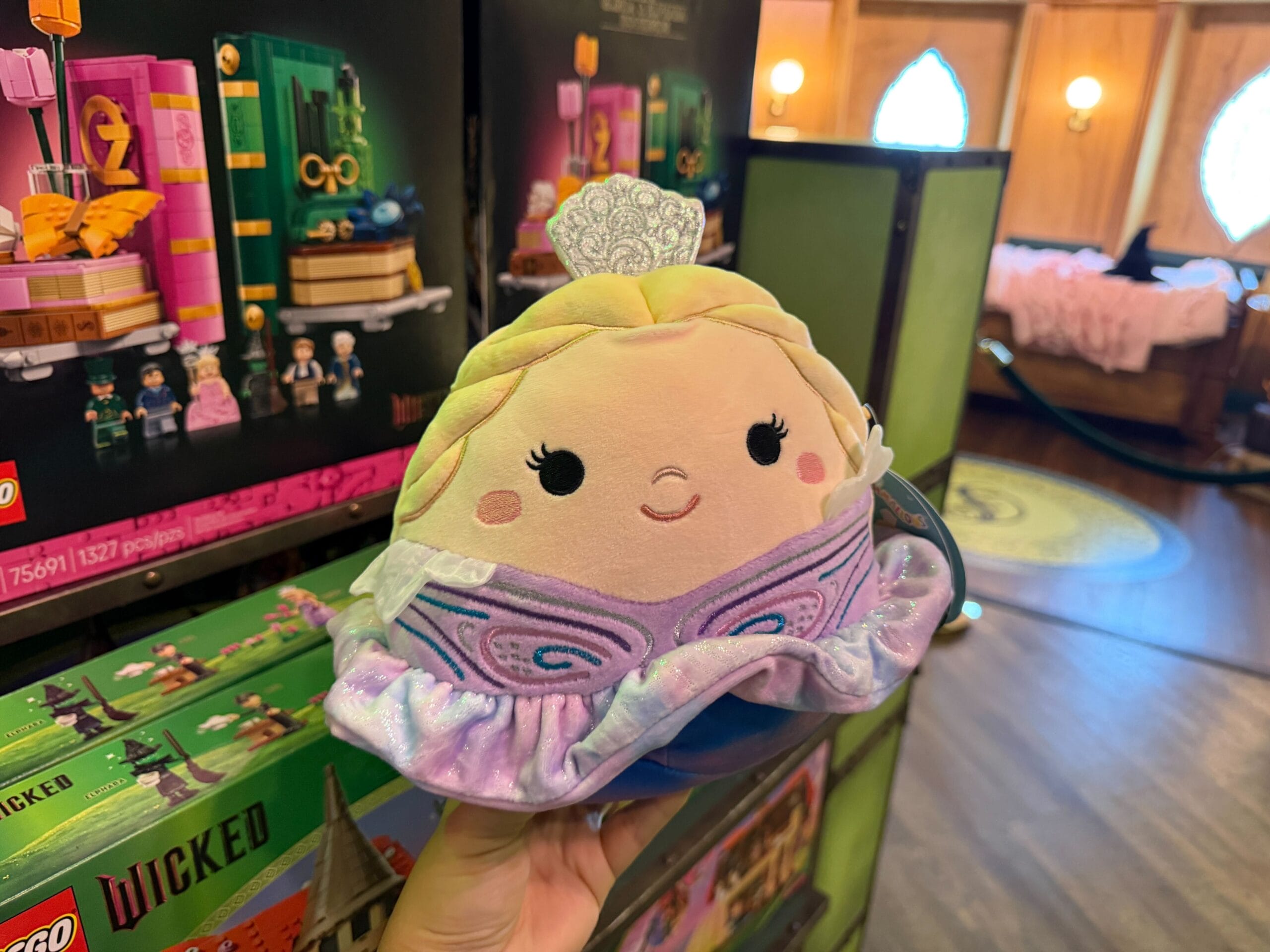 Facial details are also embroidered on the Glinda Squishmallow. She is wearing a little silver tiara, and her purple dress is embroidered with darker purple, pink, and blue details. The skirt of the dress appears to be almost like tie-dye in purple and blue tones.