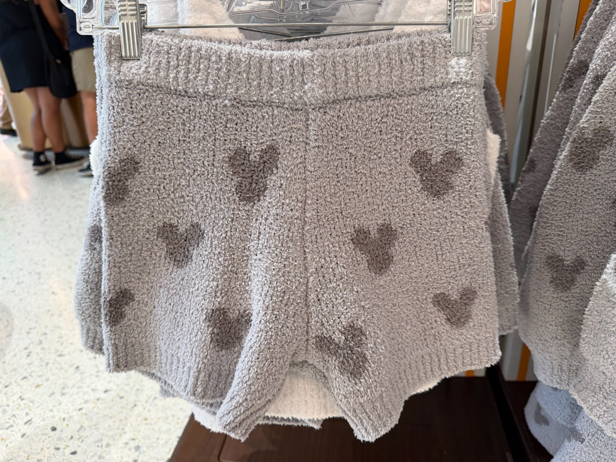 This is a two-piece set. The top is white and fuzzy with spaghetti straps and a dark grey smiling Mickey face in the center. While the bottoms are light grey shorts with dark grey Mickey head icons all over them.