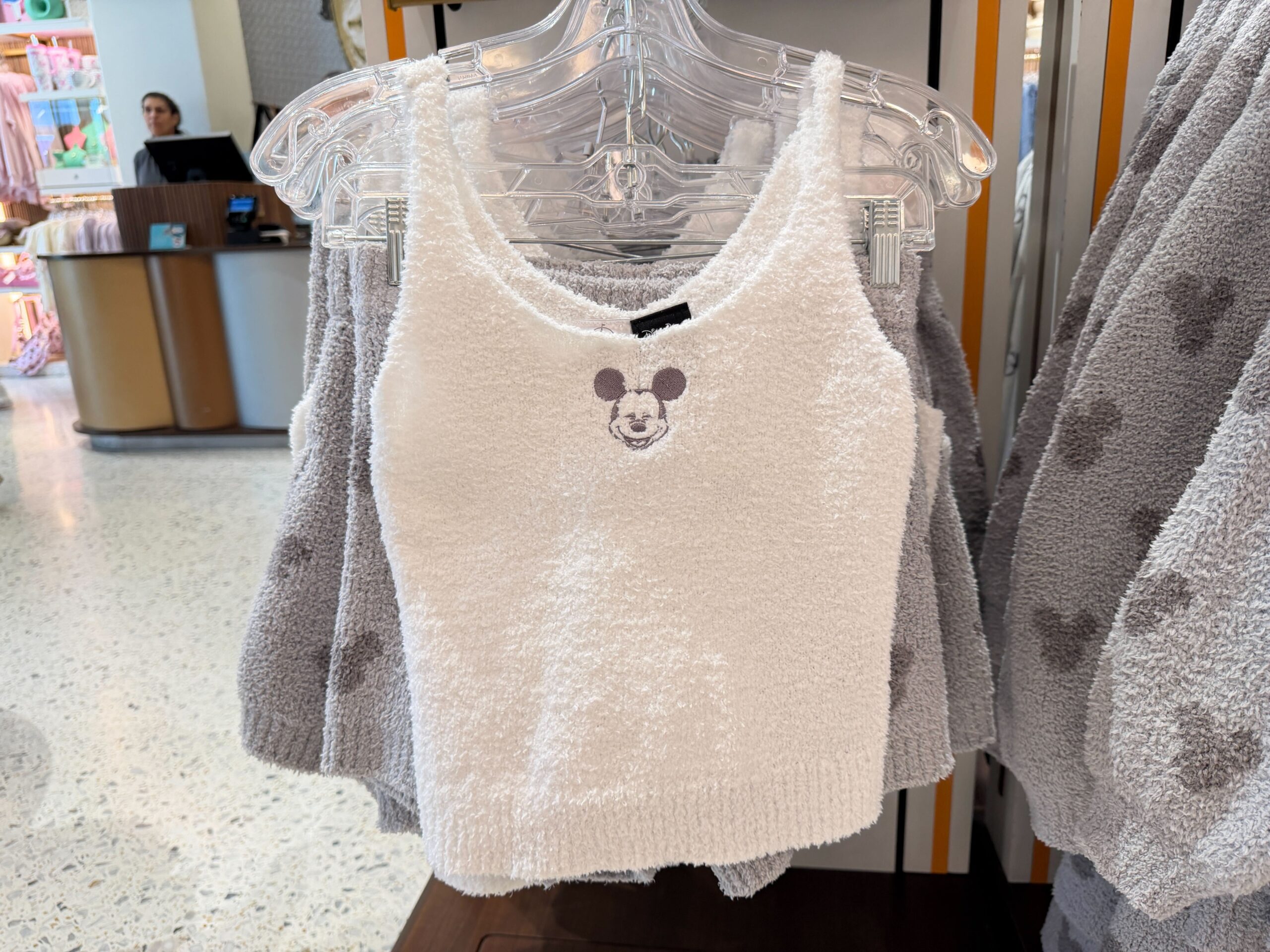 This is a two-piece set. The top is white and fuzzy with spaghetti straps and a dark grey smiling Mickey face in the center. While the bottoms are light grey shorts with dark grey Mickey head icons all over them.