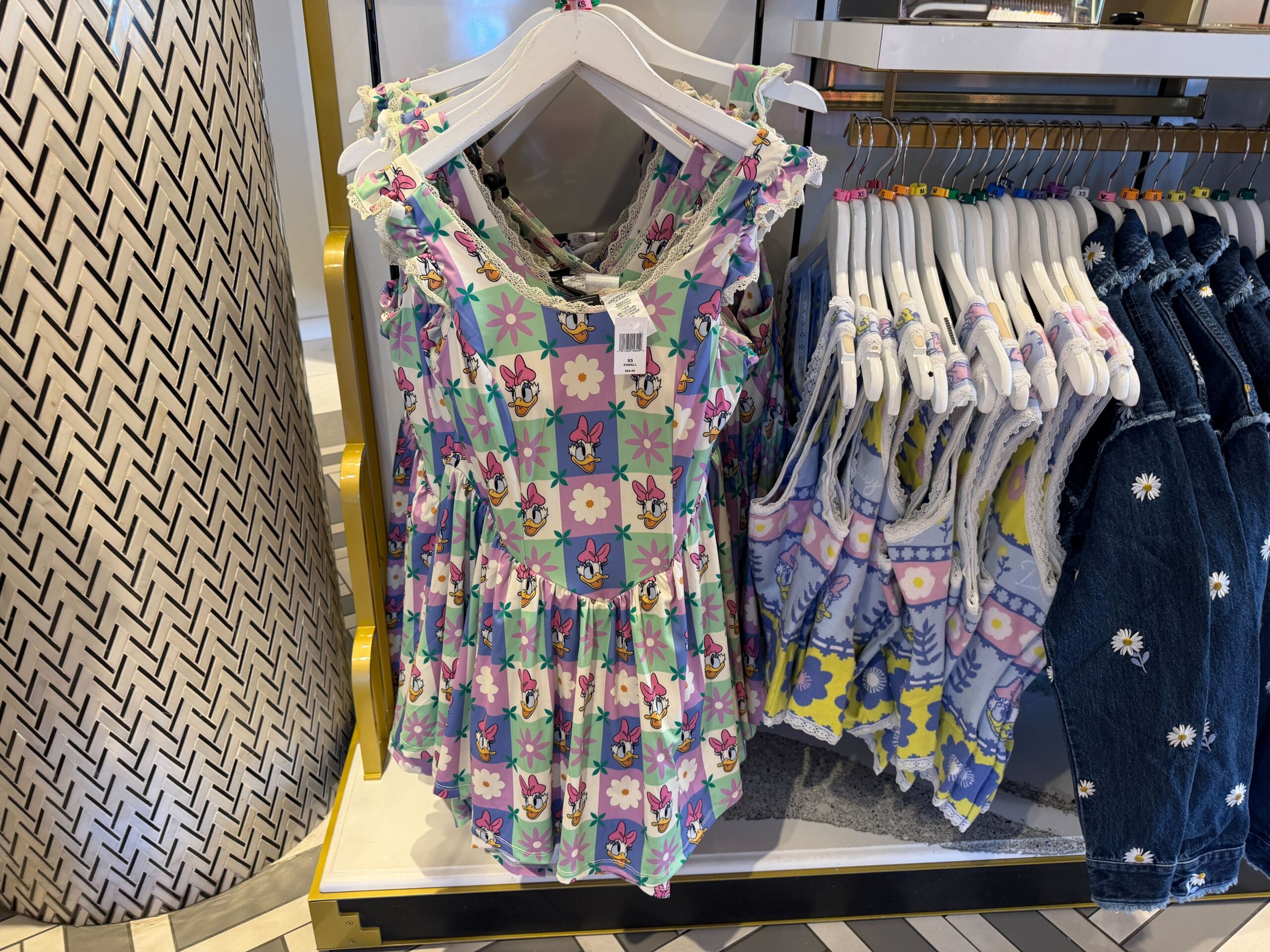 The athletic dress has built-in shorts with side pockets, a built-in sports bra with padded cups, a scoop neckline, and adjustable shoulder straps. The all-over pattern consists of multi-color checkered boxes with flowers and Daisy’s face. There is lace trim on the flutter sleeves and collar. It has a gathered skirt.