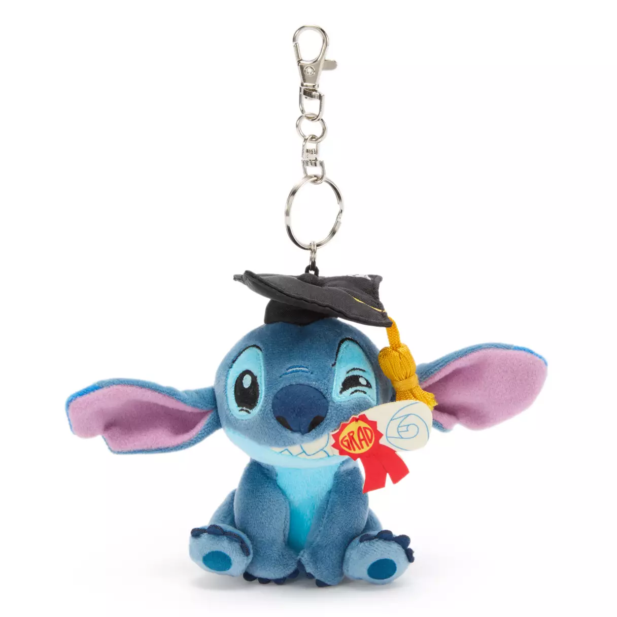 This is a mini, keychain version of the Stitch graduation plush we saw at Walt Disney World in 2025. Stitch is in his regular blue colors and sitting with a diploma clenched between his teeth. The edges of the diploma stick out from either side of Stitch’s mouth. On the right side, a red and yellow award ribbon says “Grad.”