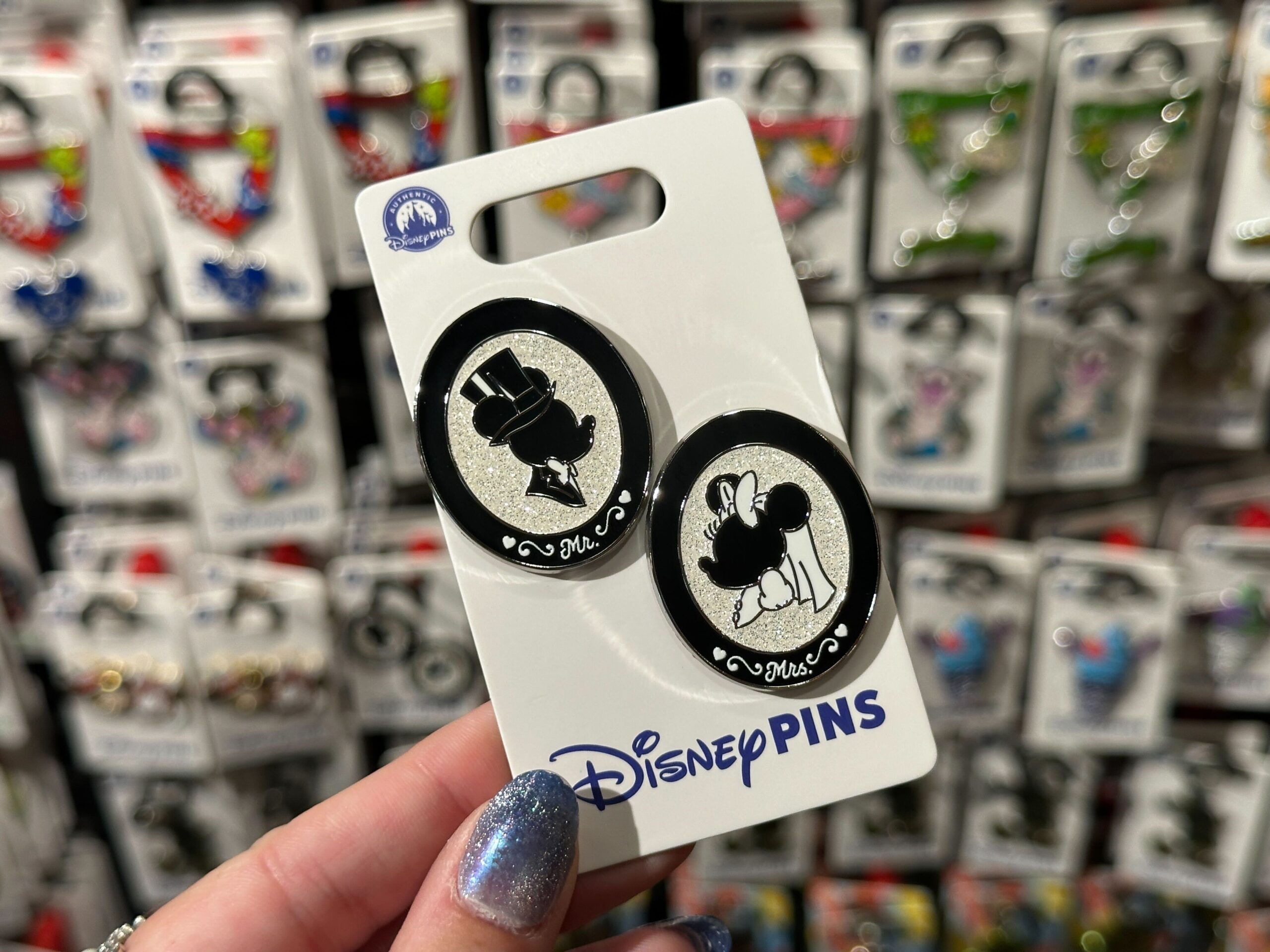 These pins are black and white with silver backgrounds. The Mickey pin depicts him in a top hat and bowtie with “Mr.” on the frame, while Minnie is in a white bow, veil, and dress with “Mrs.”