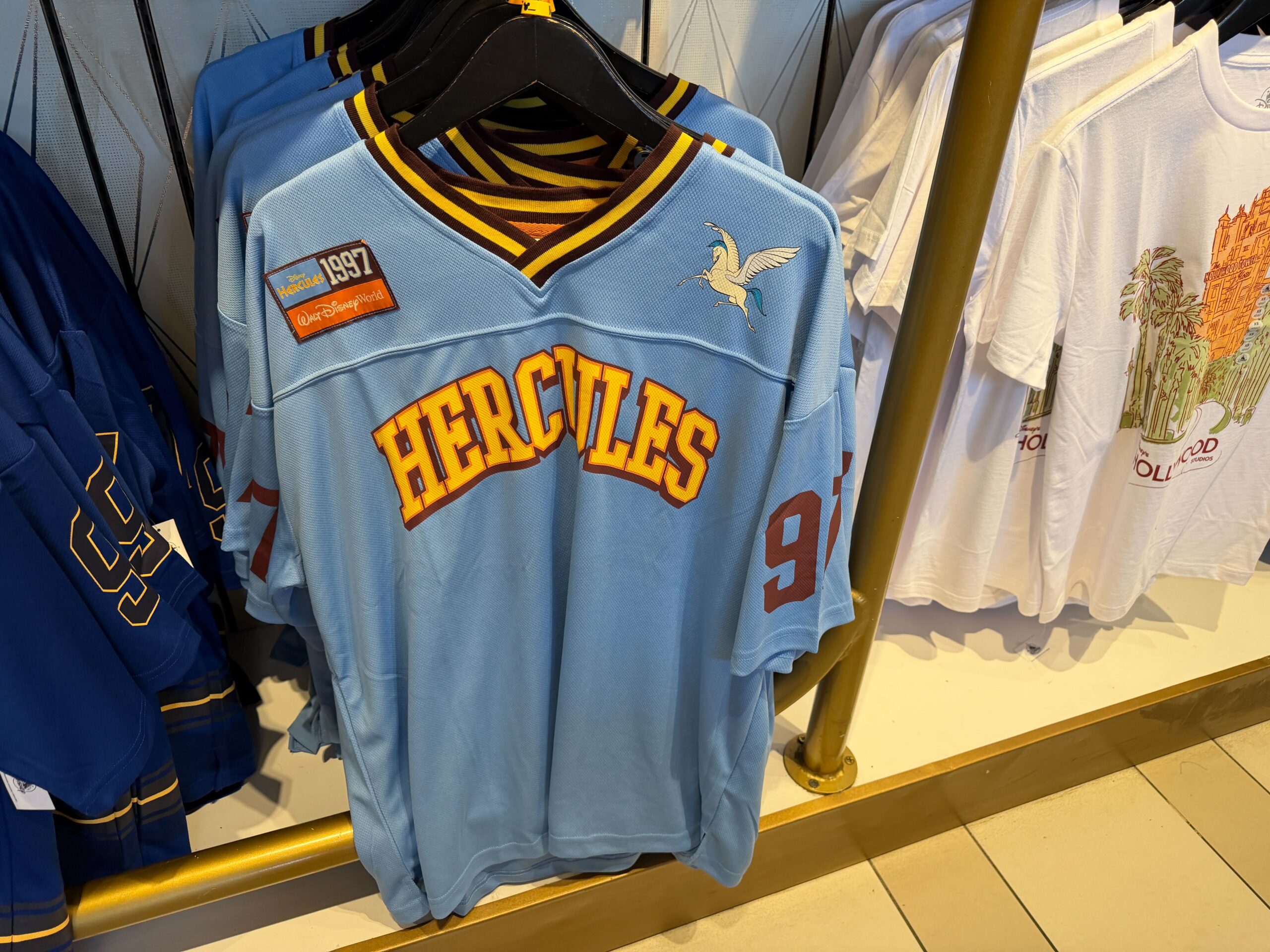 Last but not least, this Hercules jersey evokes the design of the film's titular hero. The jersey a light powder blue with burgundy and gold striping at the V-neck, and matching athletic styling. “Hercules” arcs across the chest in gold collegiate lettering in gold with a burgundy shadow, while the sleeves, right shoulder, and jersey number reflect the film's release in 1997.