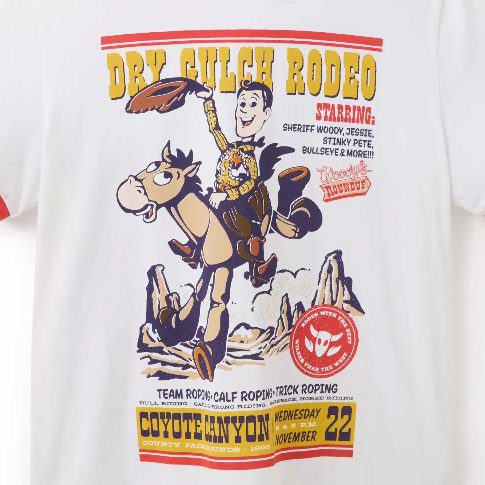 The ringer tee includes vintage poster style art of ''Dry Gulch Rodeo'' at ''Coyote Canyon County Fairgrounds'' and Woody and Bullseye. The collar and sleeves have red contrast hems.