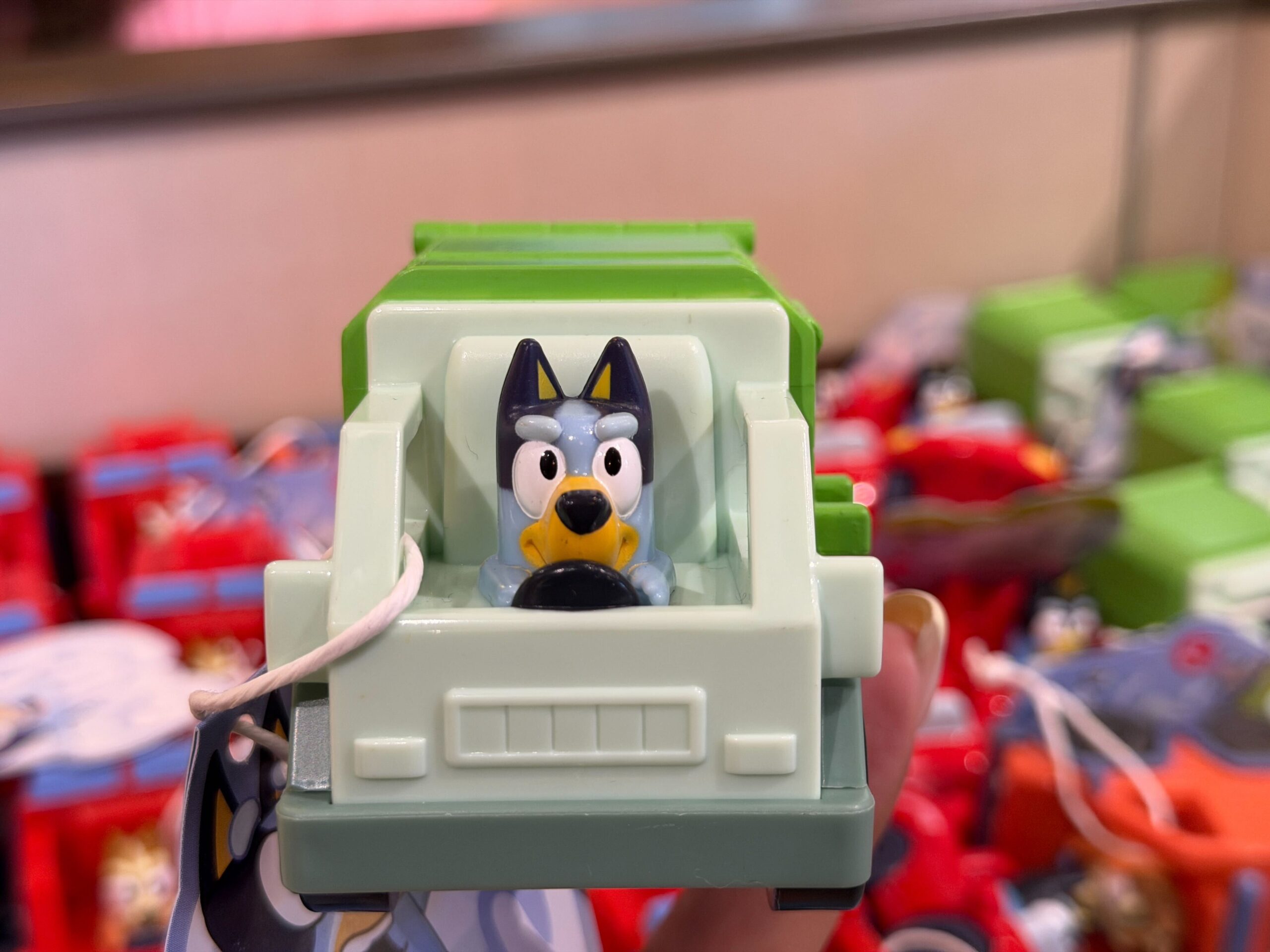 Bluey is behind the wheel of a green and gray garbage truck.