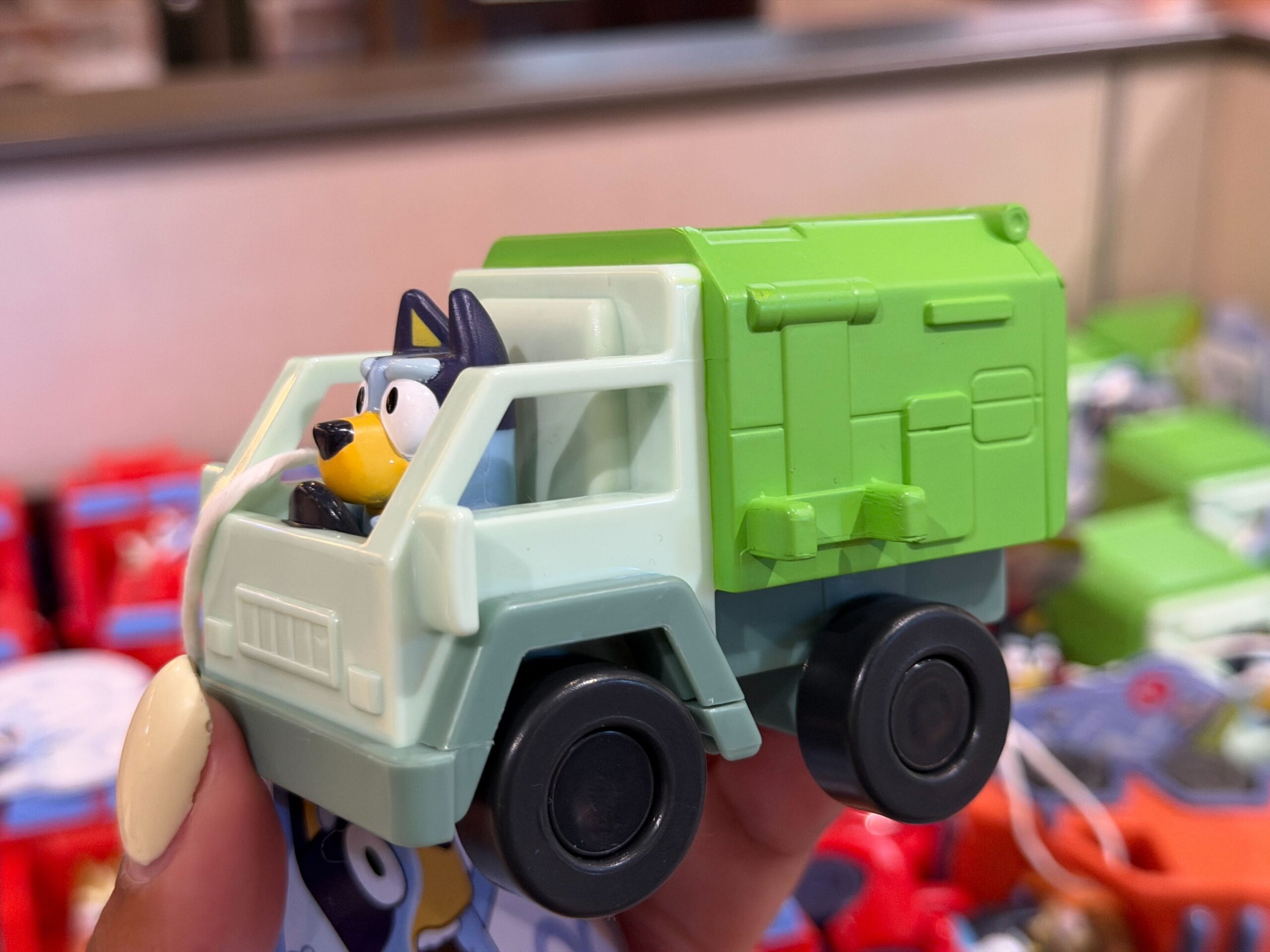 Bluey is behind the wheel of a green and gray garbage truck.
