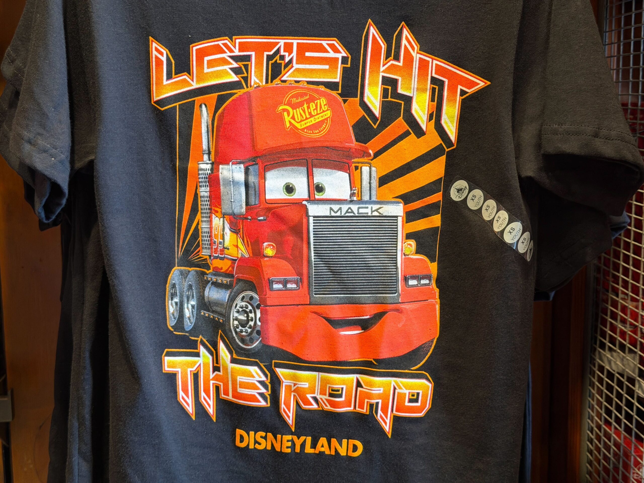 Lightning's friend Mack is on this black tee with red-orange text reading "Let's hit the road." The Disneyland wordmark is in orange at the bottom.