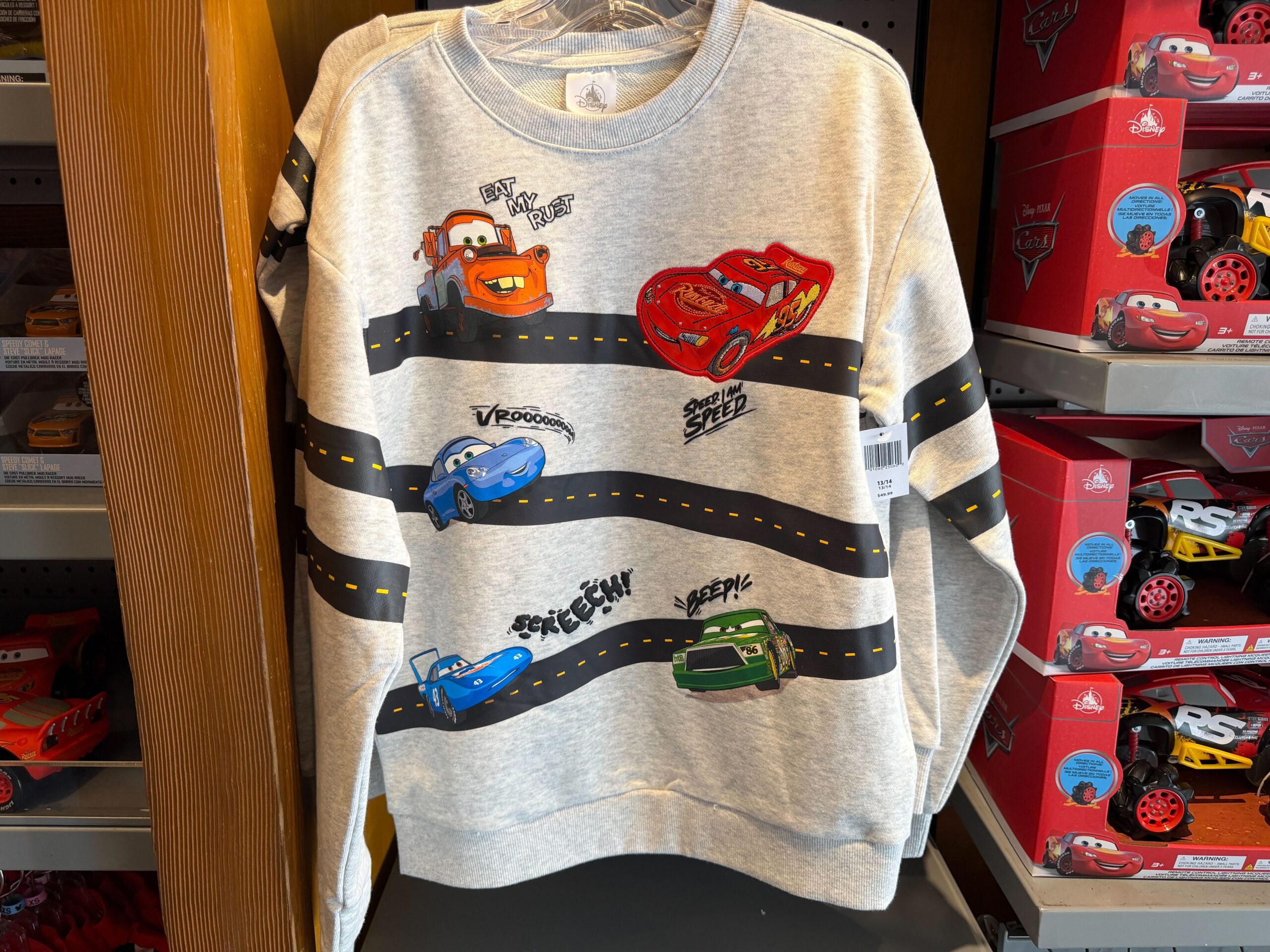 The heathered sweatshirt features wavy roads across the chest and sleeves. Various Cars characters are pictured driving: Mater, Lightning, Sally, Strip Weathers, and Chick Hicks.