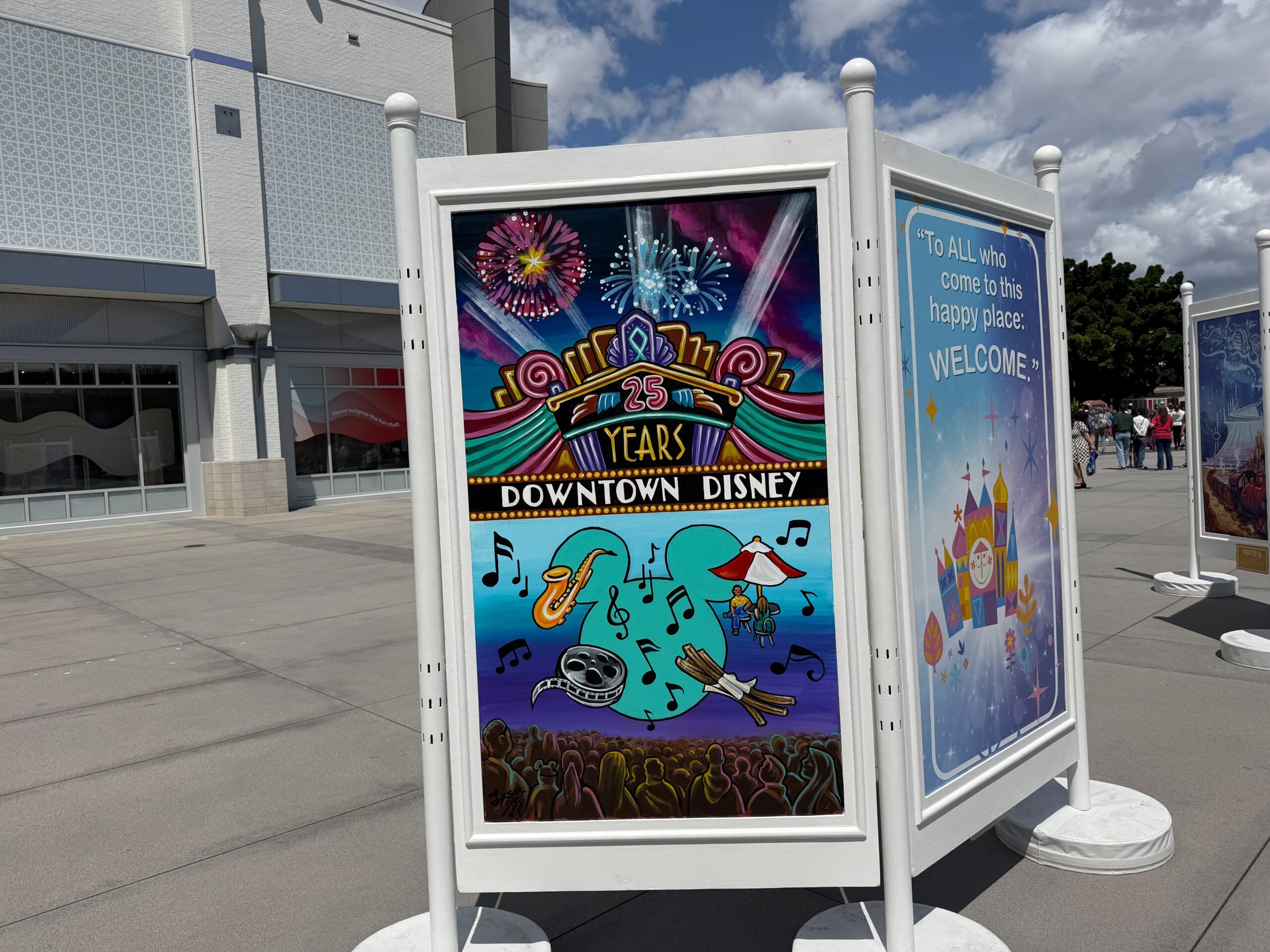 Another display has "To ALL who come to this happy place: WELCOME." and a scene of Downtown Disney's 25th anniversary.