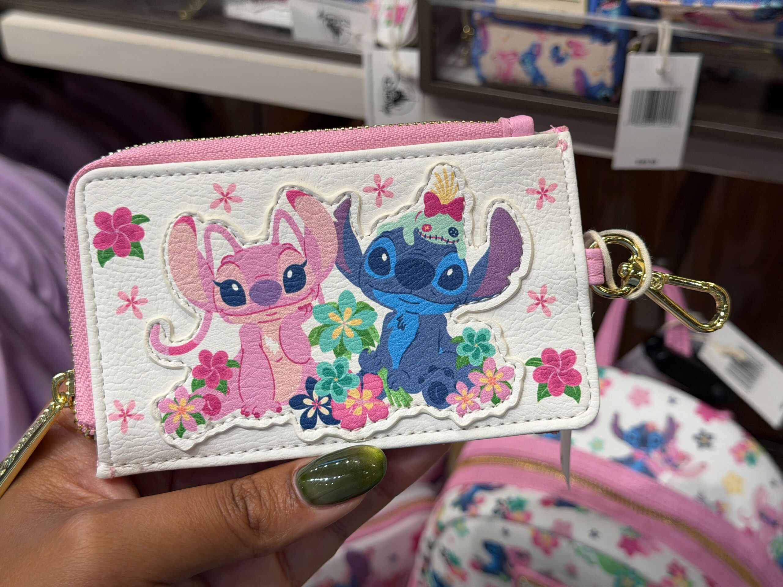 This white Loungefly wallet has a design of Angel and Stitch sitting side-by-side while multicolored tropical flowers surround them. Scrump sits on Stitch’s head.