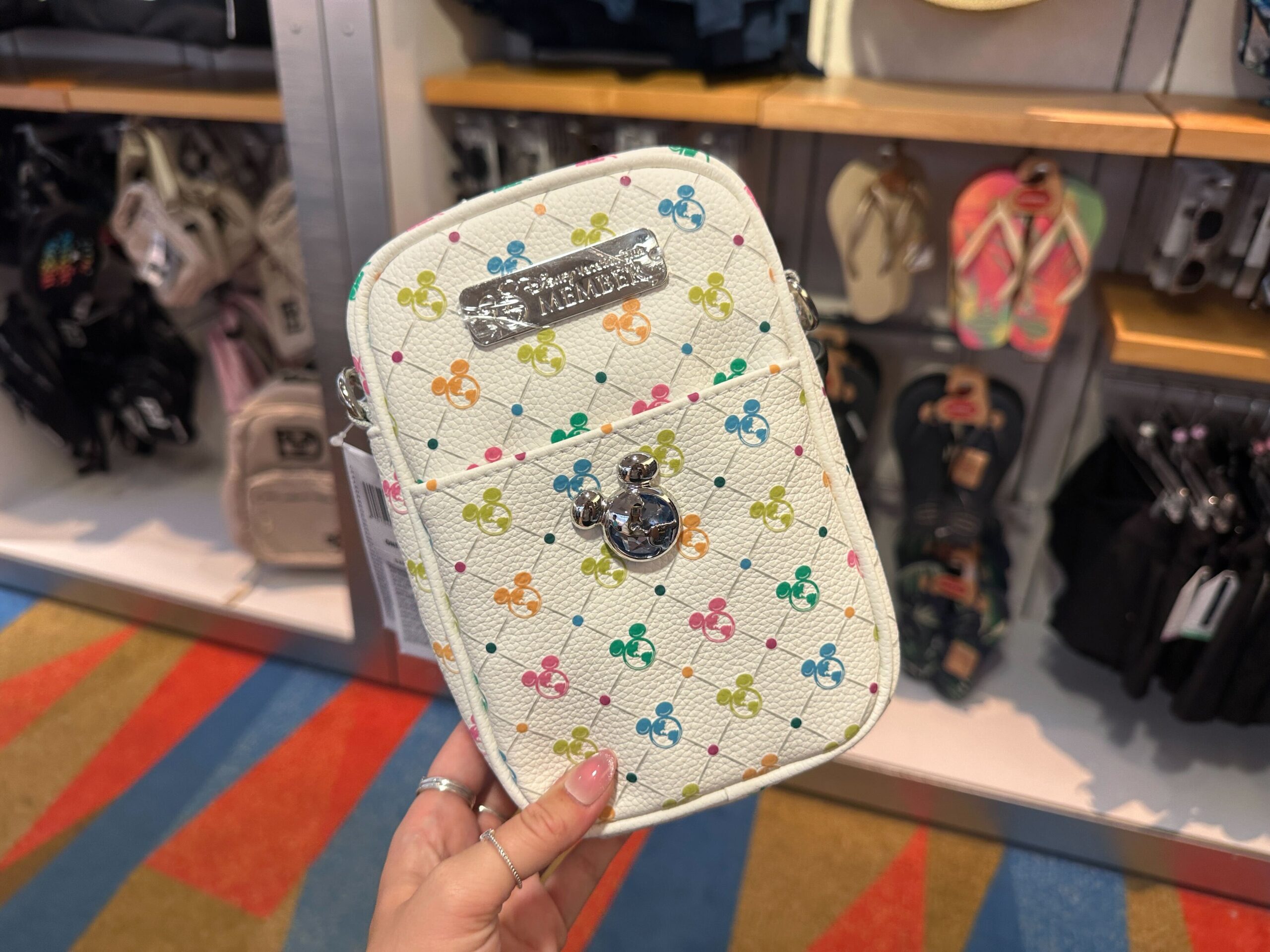 The same pattern from the ear headband is repeated across the front, back, and sides of this white crossbody bag. A silver Mickey globe icon is on the front of the outer pocket. A silver metal "Disney Vacation Club" badge is at the top of the front.