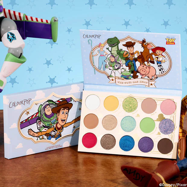 The Toys Are Here Shadow Palette includes 15 shades in matte, metallic, matte sparkle, and pearlescent glitter finishes. Each shadow is inspired by a character, with names like "Intergalactic," "Rex Flex," "Falling with Style," "Bo Peep Blue," and "Howdy, Partner." The outside cover of the palette features an image of Buzz Lightyear holding onto Woody, "falling with style" right into Andy's box of toys. The inside cover reveals an image of the gang striking their iconic poses.