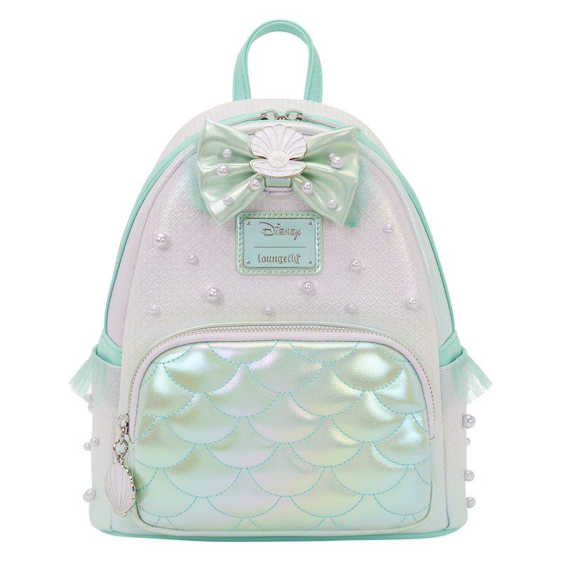 The polyurethane exterior has an iridescent fish scale pattern. Teal green trim is around the zipper and in the side slip pockets. A 3D bow with an enamel seashell charm is on the front, above the cloisonné Disney | Loungefly label plate.