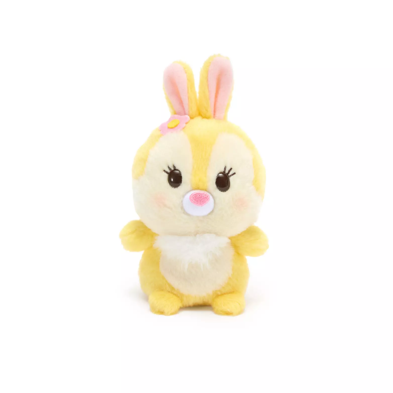 Miss Bunny is made from a vibrant yellow plush material with a tuft of white fluff beneath her chin. Her eyes are 3D brown appliques with embroidered eyelashes, while her nose is embroidered in pink. There is a slight pink blush to her cheeks, and she has a small pink flower next to her right ear.