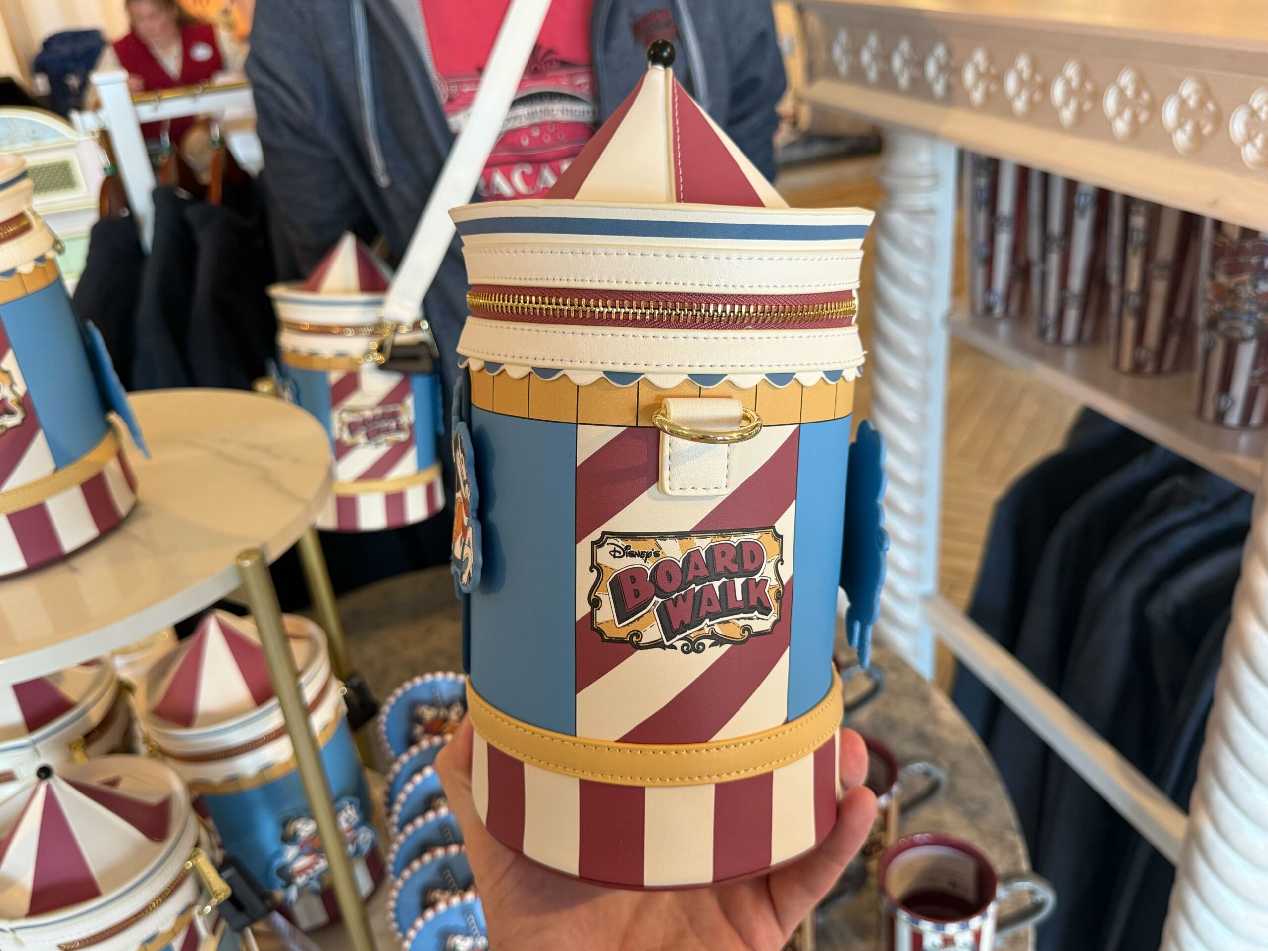This Loungefly bag is in the shape of a circus tent. It is blue with red and white stripes and yellow details. One one side is an applique of Mickey riding a carousel, and the other side has the BoardWalk wordmark.