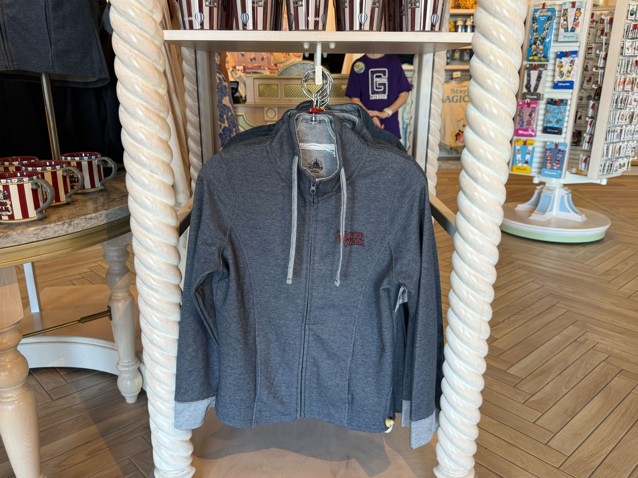 The heather blue zip-up jacket has the resort wordmark on the chest in red text. The strings, sleeve cuffs, and interior lining are a light blue striped color.