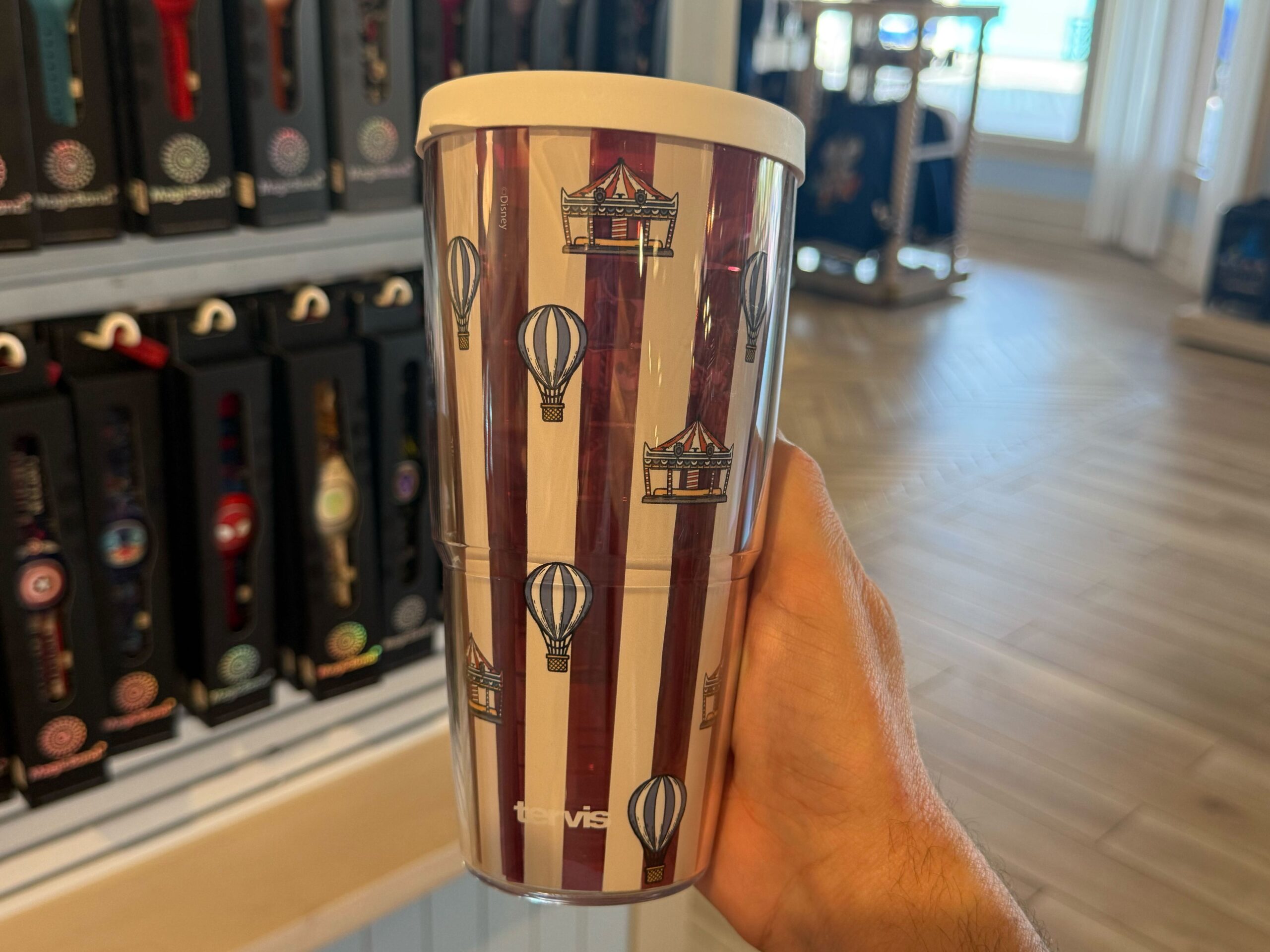 There is also a travel tumbler in this collection, which has red and white vertical stripes. An image of Mickey and Minnie riding carousel horses is on one side, while an allover pattern of carousels and hot air balloons surround the rest. The lid is white.