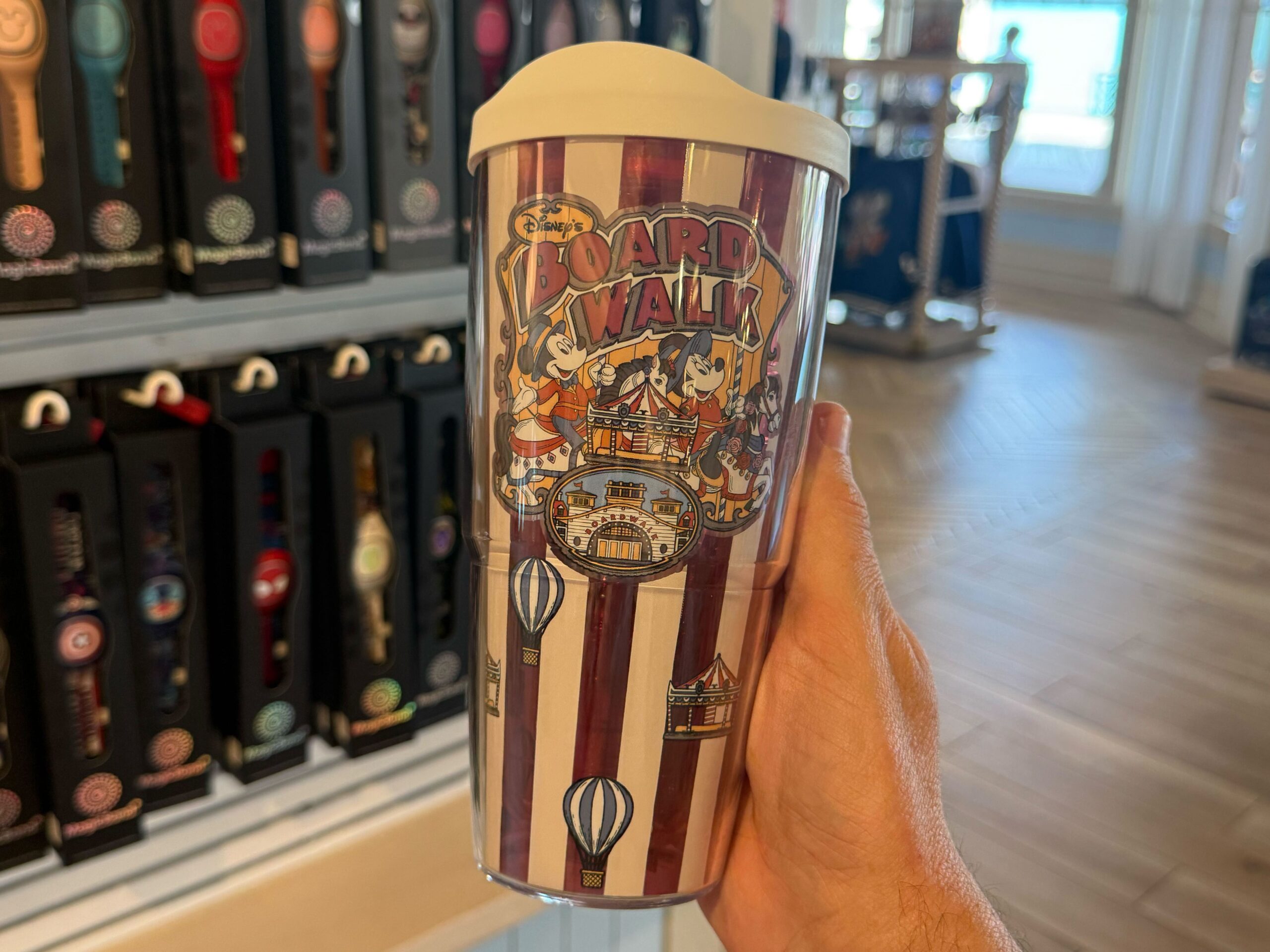 There is also a travel tumbler in this collection, which has red and white vertical stripes. An image of Mickey and Minnie riding carousel horses is on one side, while an allover pattern of carousels and hot air balloons surround the rest. The lid is white.