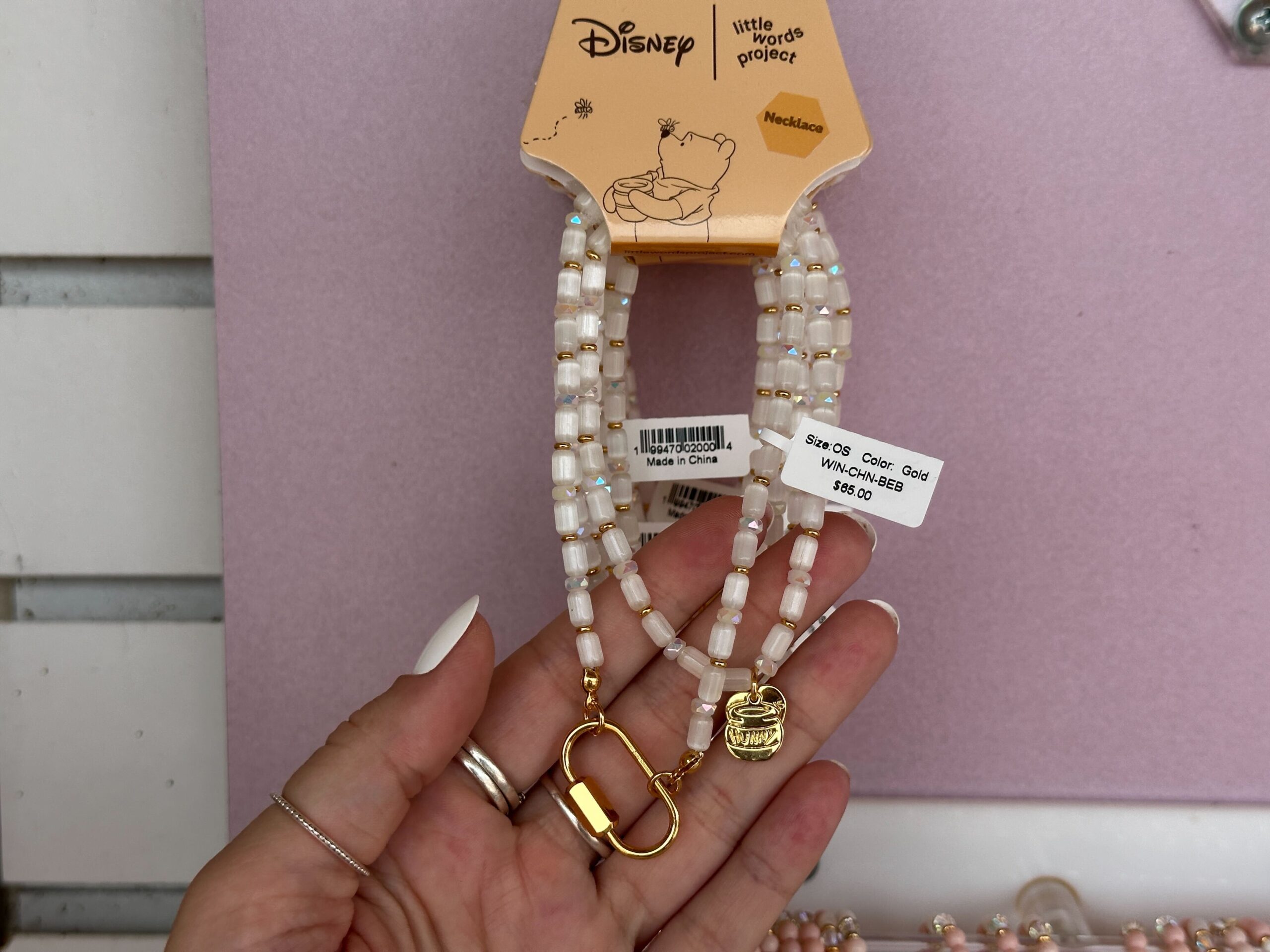 This necklace has white pearlescent beads and a gold-tone hunny pot charm at the end. There is also a place to add charms.