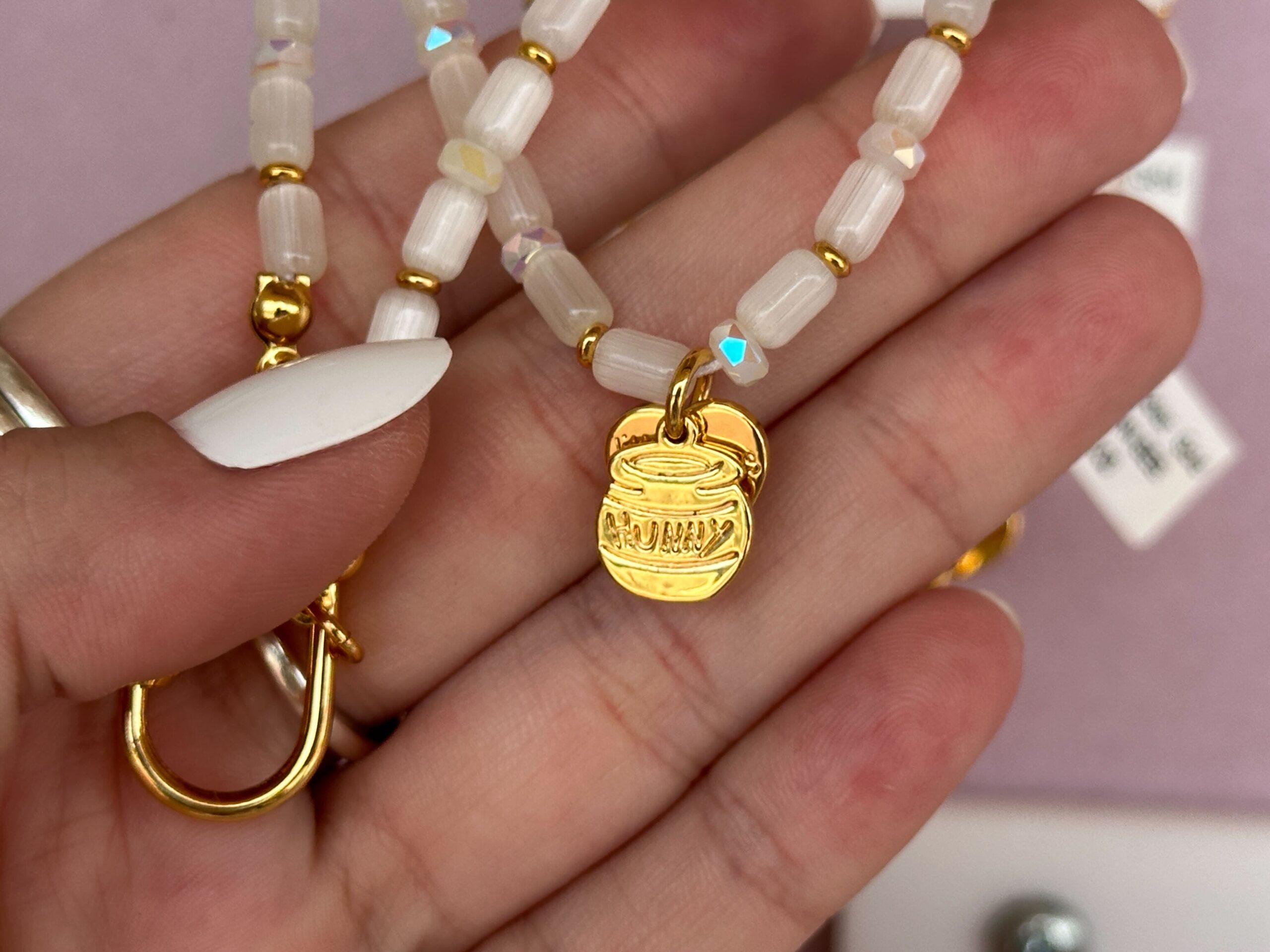 This necklace has white pearlescent beads and a gold-tone hunny pot charm at the end. There is also a place to add charms.