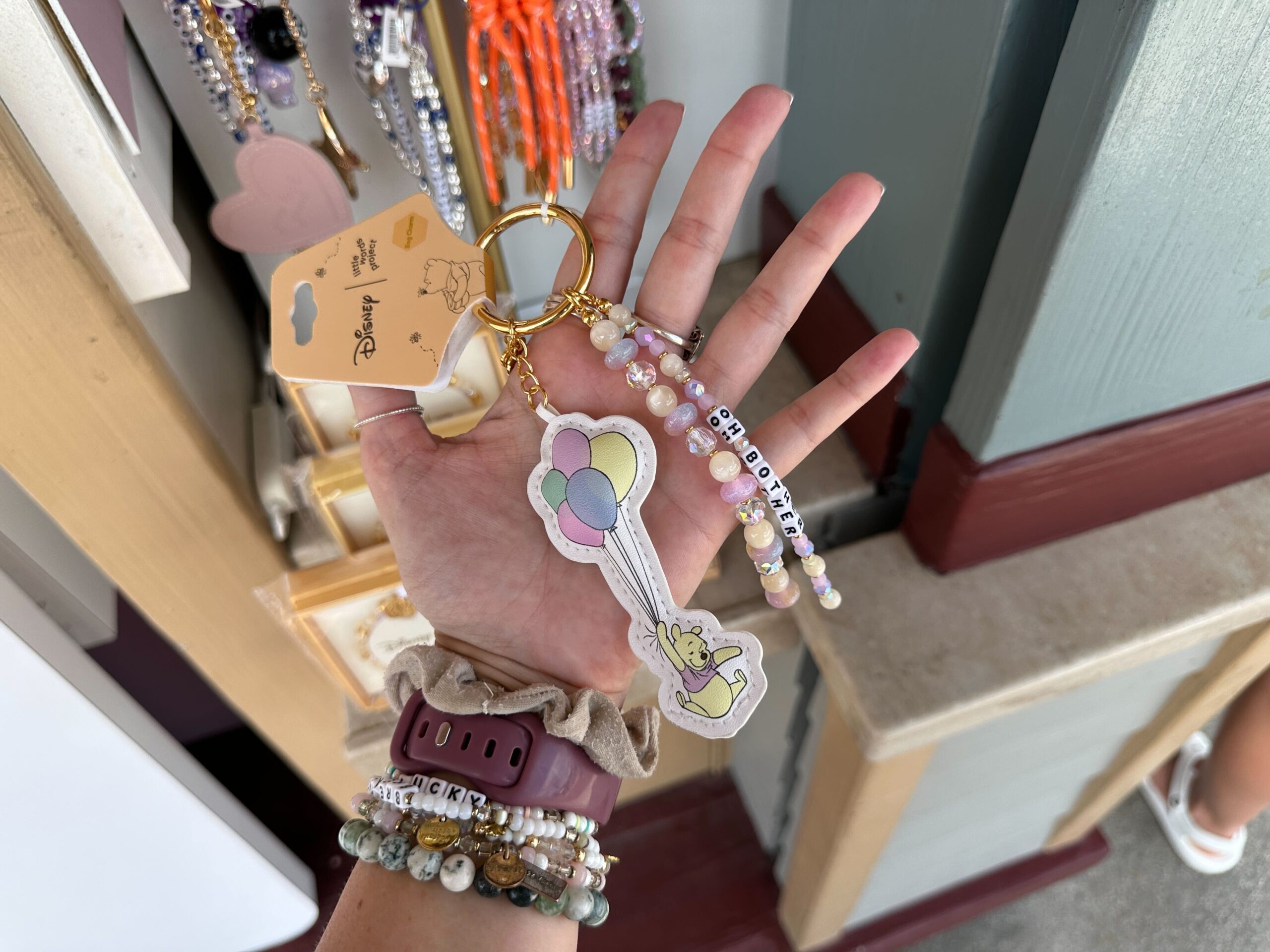 The featured bag charm includes three strands of Pooh-inspired designs: one with Pooh happily floating around by way of a handful of large balloons, one strand that includes the brand’s signature friendship-bracelet letter beads spelling the bear’s signature “oh bother”, and a third simple touch consisting of the alternating bead designs between the larger Pooh motifs.