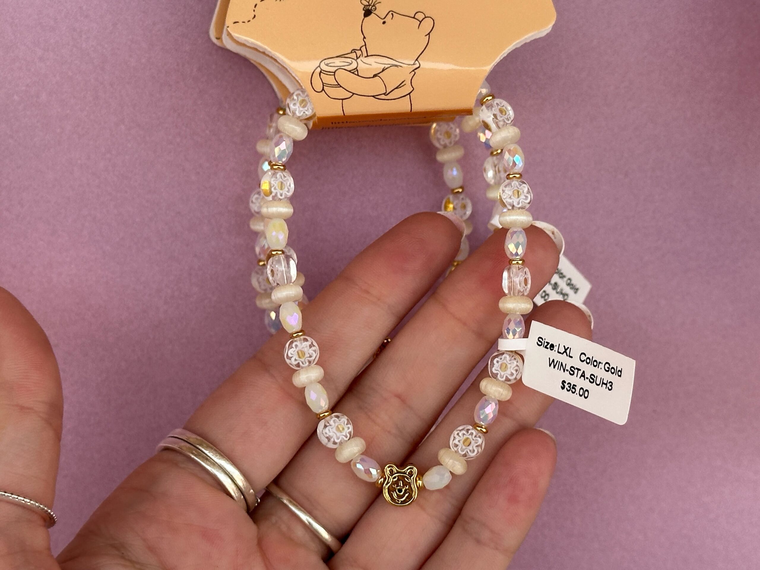 At the back of the bracelet is a dangling Pooh charm. The beads in this bracelet are white with floral accents, gold, ivory, or pearlescent.