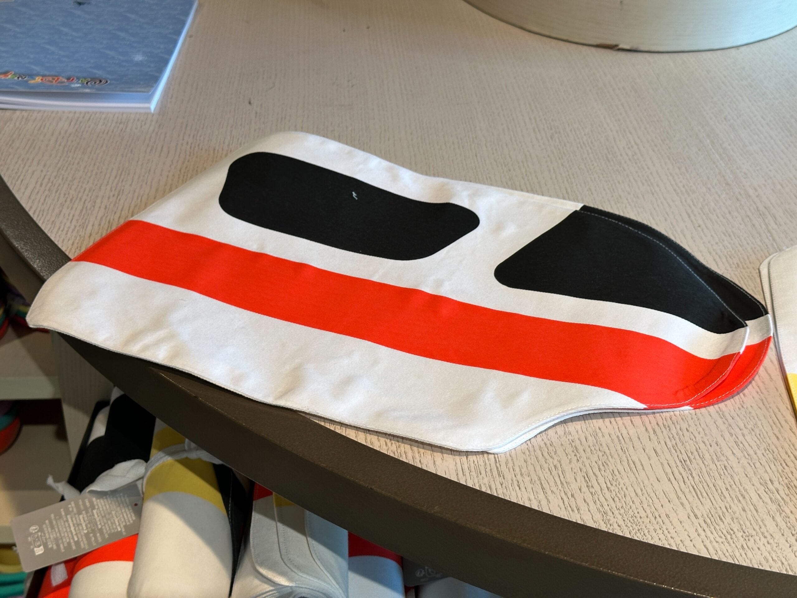 The fabric placemat is in the shape of a Monorail car, with the blacked out windows and red stripe that runs along the side.