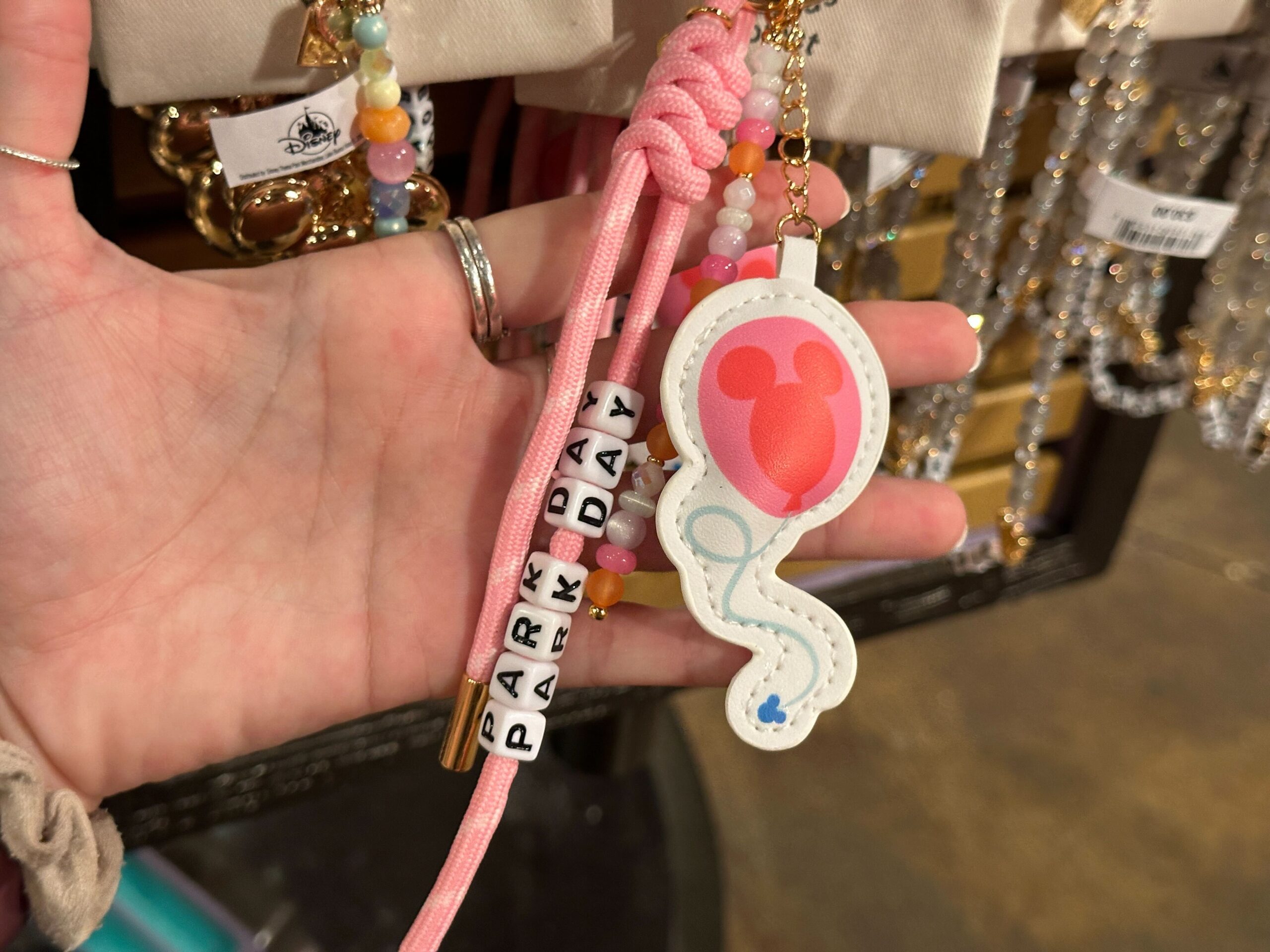 The "Park Day" bag charm is made of pink paracord. A Mickey-shaped balloon charm dangles from the keychain. Another strand has orange, pink, and pearly white beads.