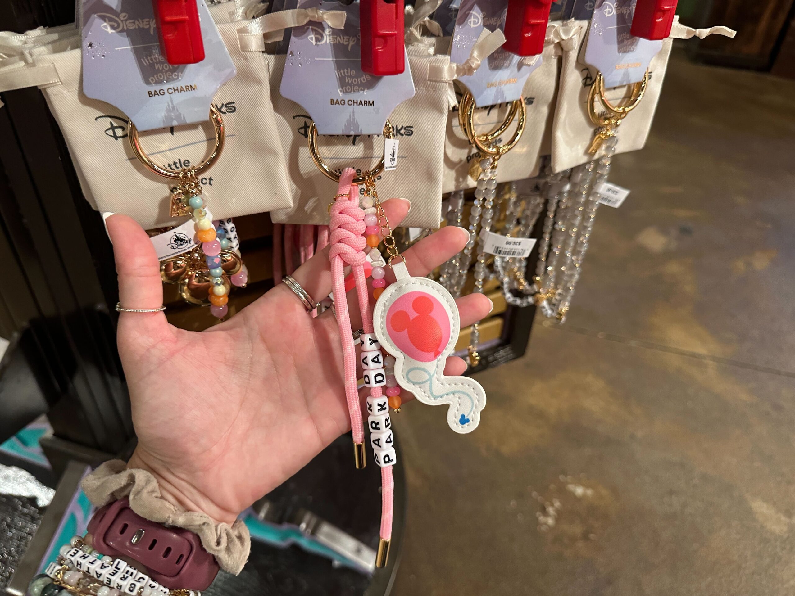 The "Park Day" bag charm is made of pink paracord. A Mickey-shaped balloon charm dangles from the keychain. Another strand has orange, pink, and pearly white beads.