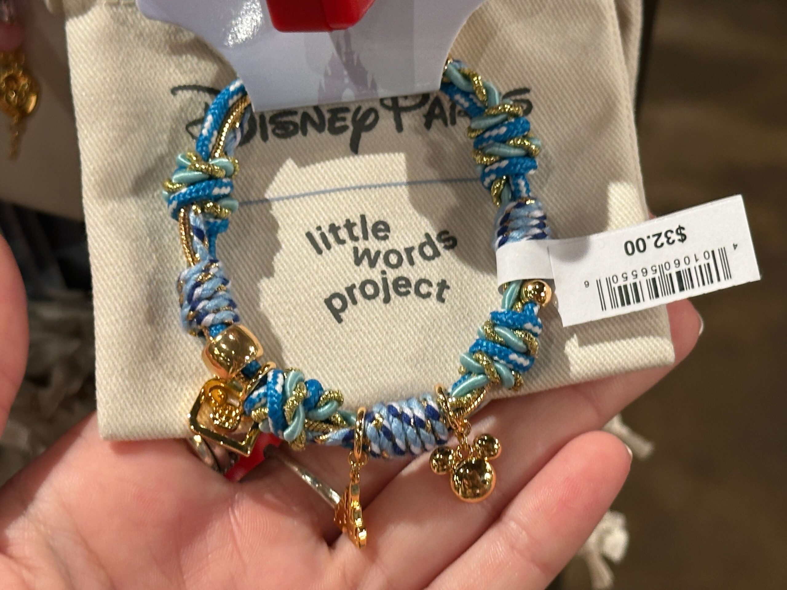 This bracelet has several different kinds of blue and glittery gold paracord wrapped around it. Charms include a Mickey icon, Fantasyland castle, and D logo.