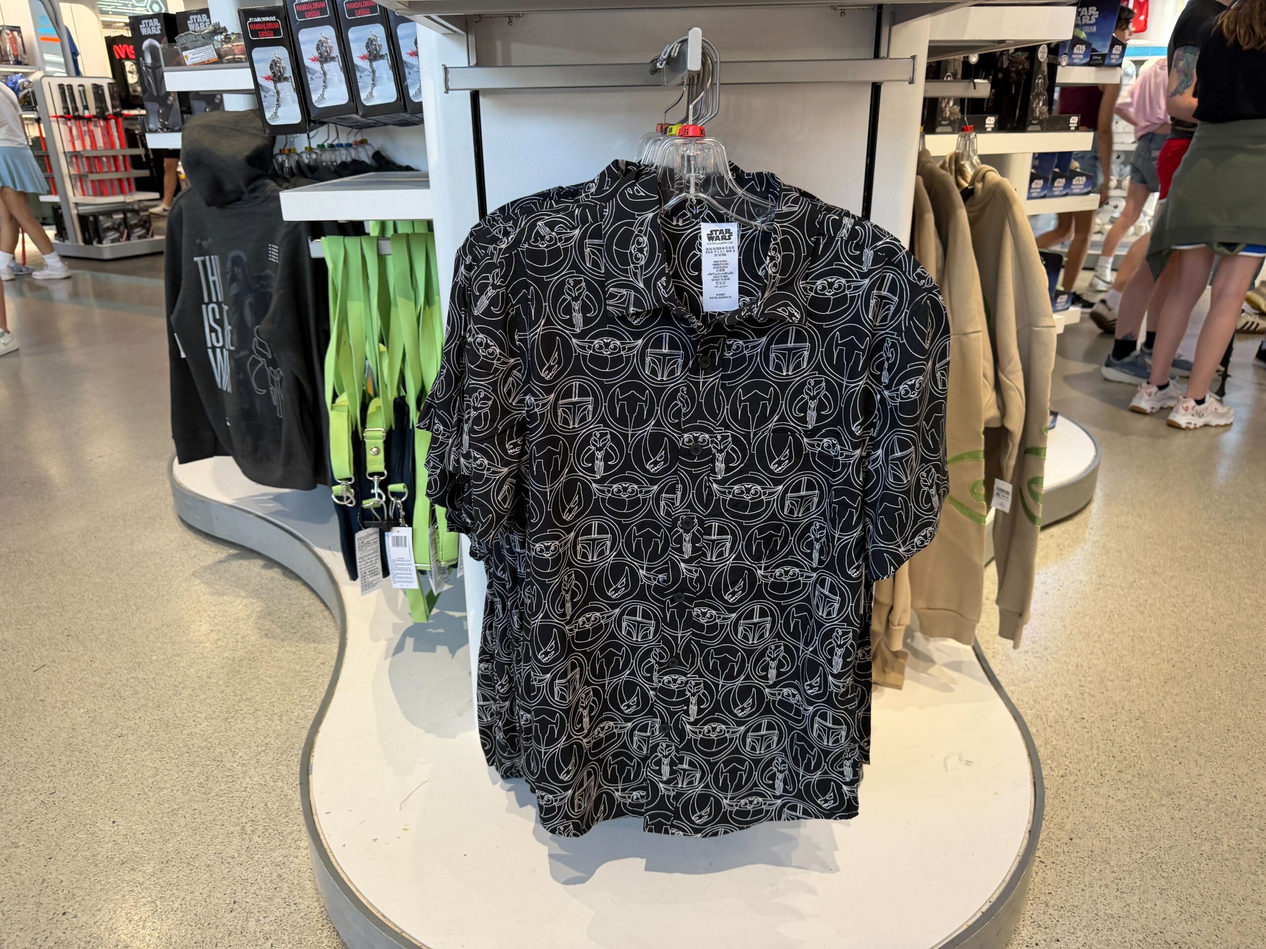 The button-up is black with an all-over white pattern featuring Grogu in his pram, Mando's helmet, the mythosaur skull, the mudhorn symbol, and Mando's N-1 starfighter.