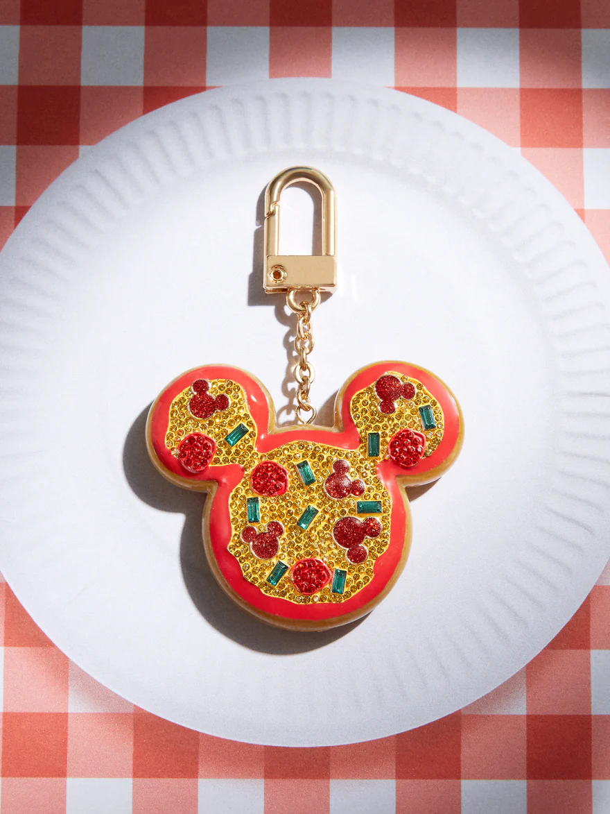 A bag charm in the shape of a pepperoni pizza. The pizza is in the shape of a Mickey Mouse head, and some of the "pepperoni" toppings are also shaped like Mickey's head.