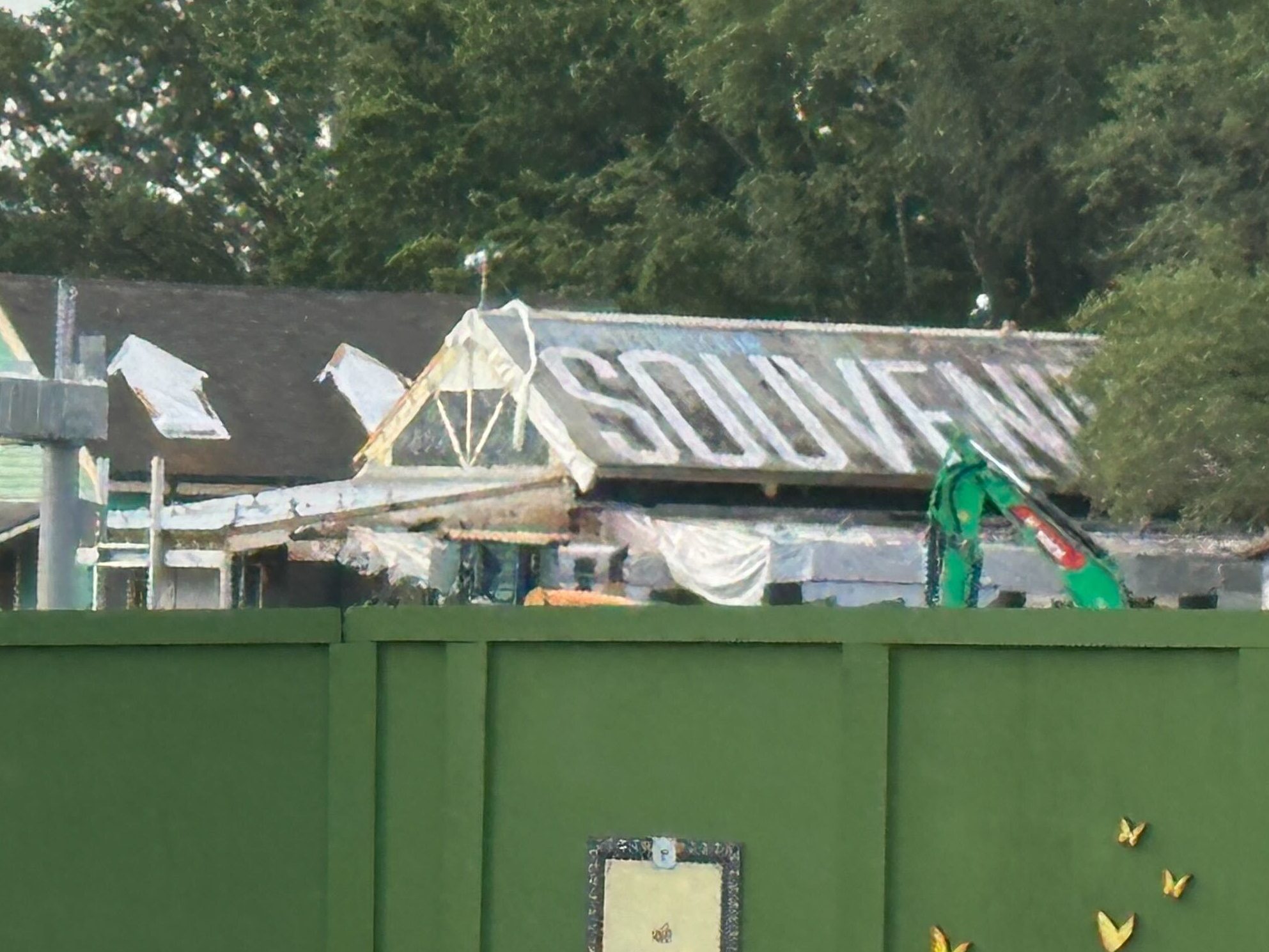 Construction equipment surrounds the building, which now has a lot of tarps covering various parts of it. There is protective plastic installed on the skylight windows on the left building, and tarps completely covering the top of the porch overhang on the right building. All of the metal signposts have also been removed from the rooflines and awning overhang.