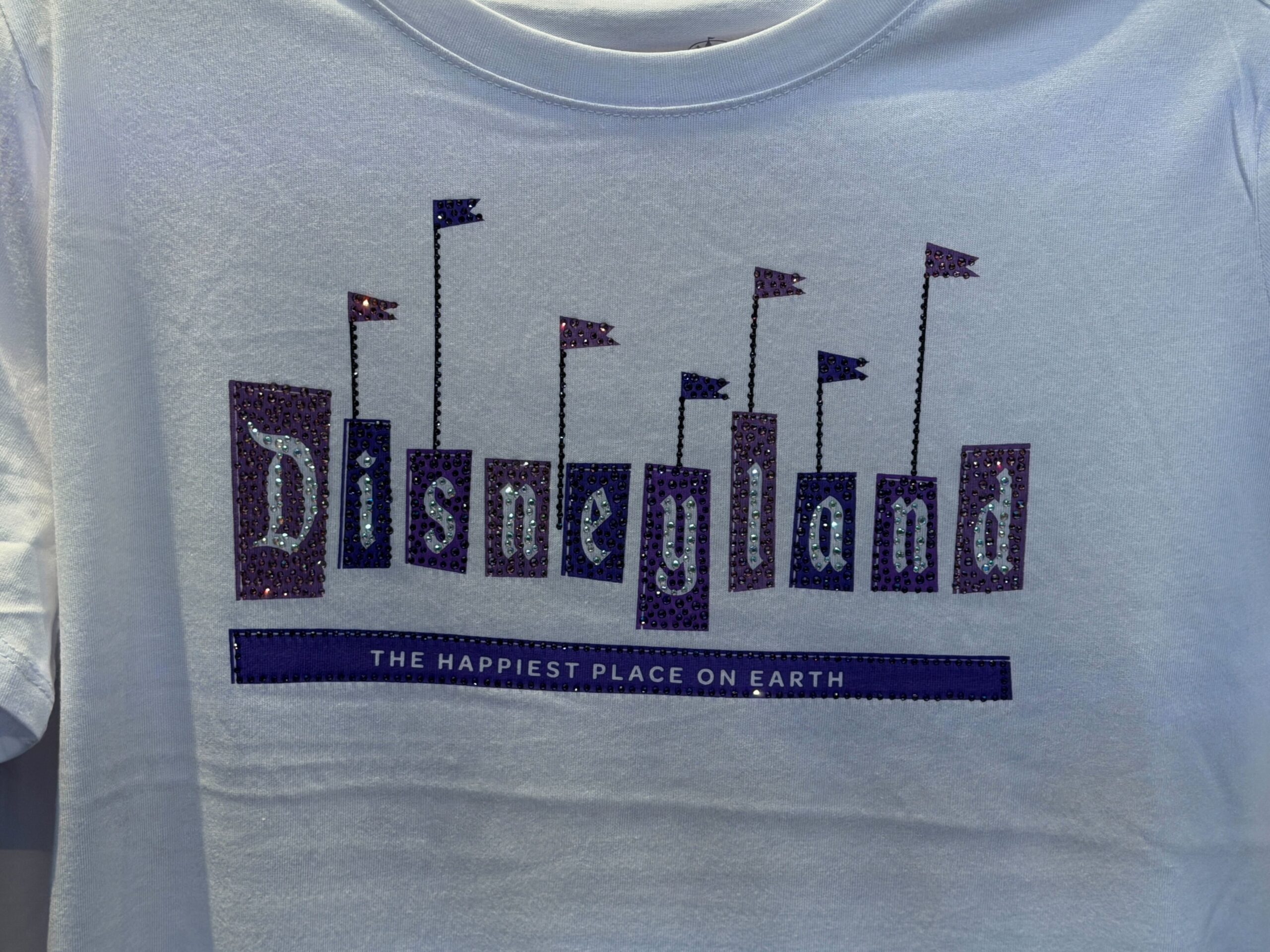 This light purple shirt features the Disneyland 70 logo on the left chest. Silver puffy ink and rhinestone accents highlight the logo.