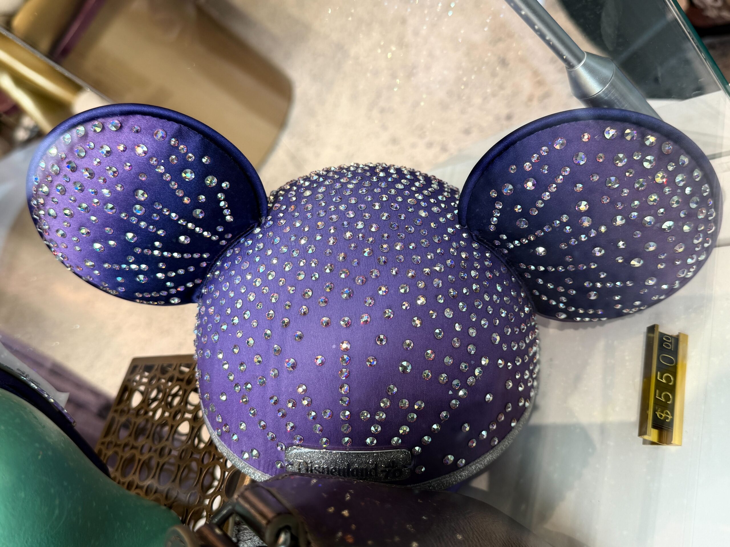 The ear hat is a rich purple with real Swarovski crystals across the cap and ears. A glittery silver Disneyland 70 plaque is on the front.