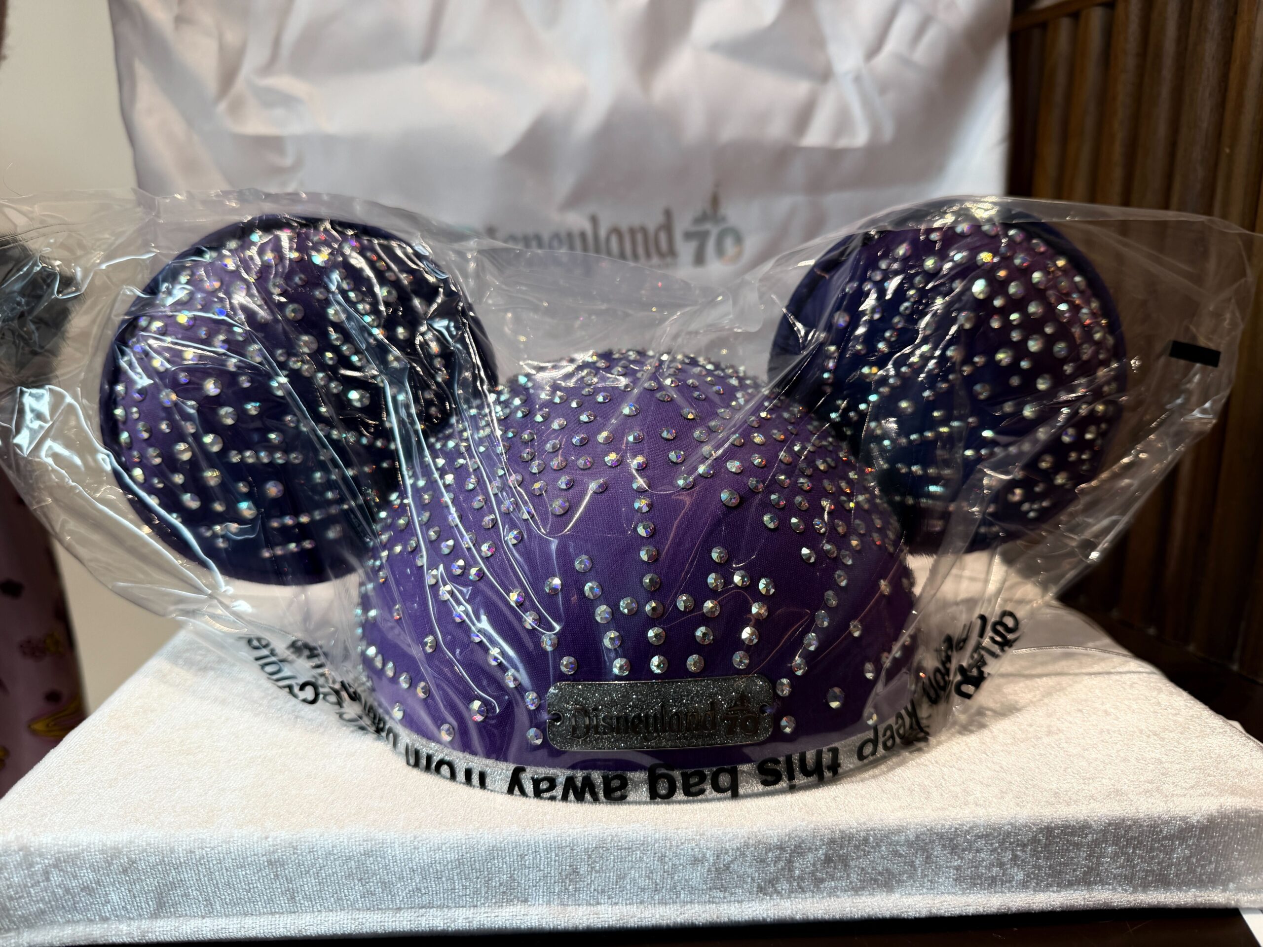The ear hat is a rich purple with real Swarovski crystals across the cap and ears. A glittery silver Disneyland 70 plaque is on the front.