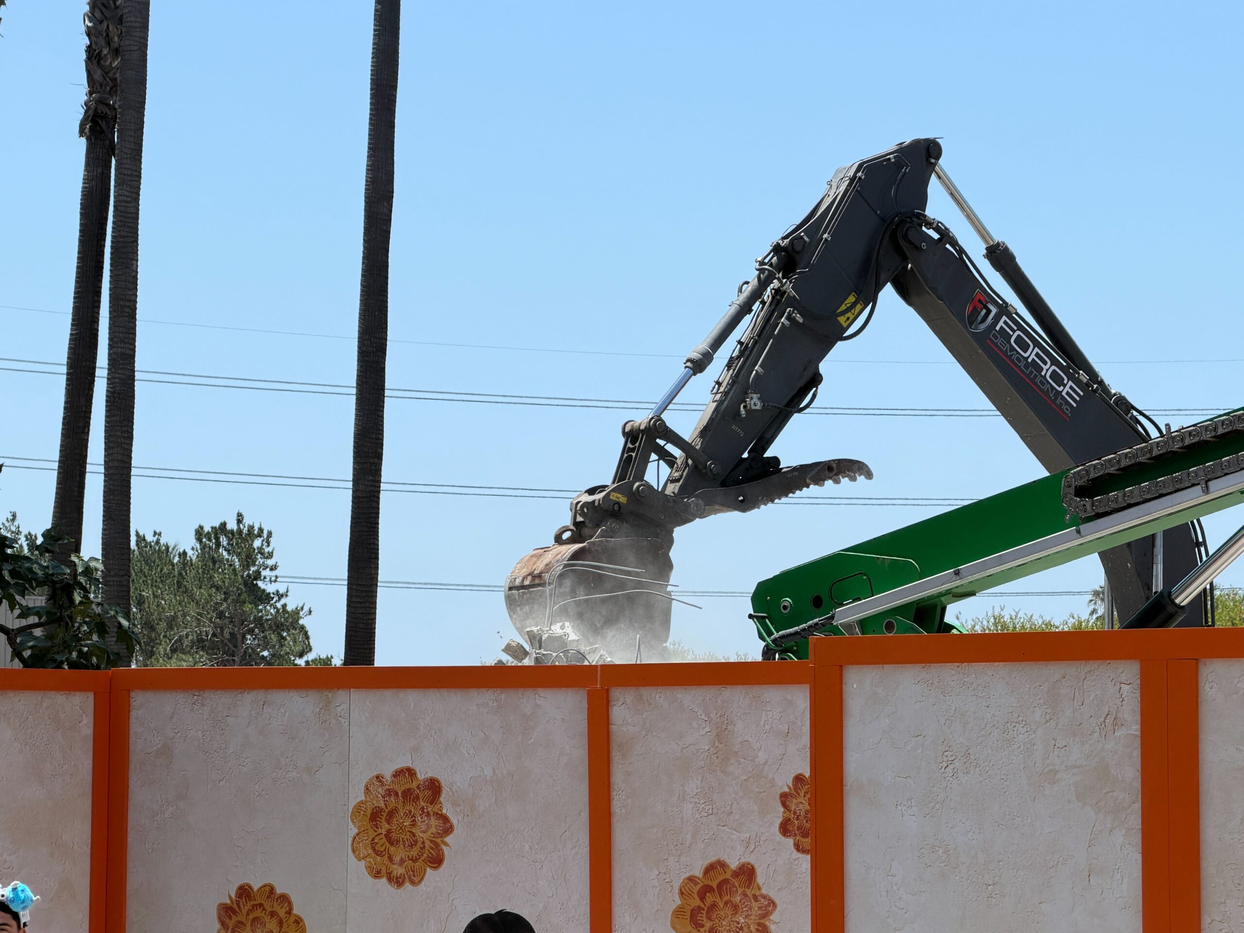 The bucket reached around to the back of the concrete wall and pulled it down, creating a small cloud of dust.