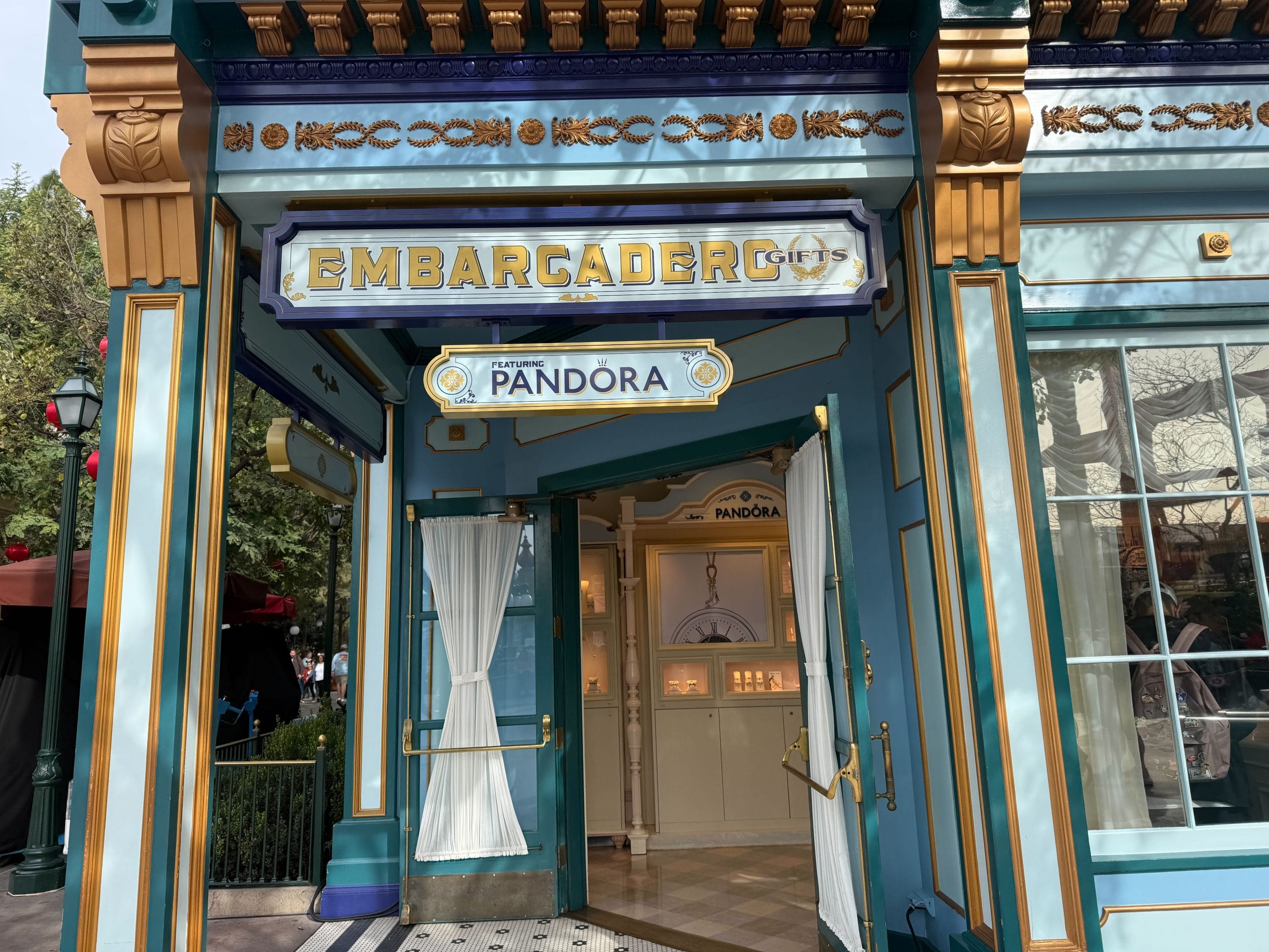 Embarcadero Gifts facade at Disney California Adventure featuring an ornate blue and gold exterior with a sign saying, "Featuring Pandora."