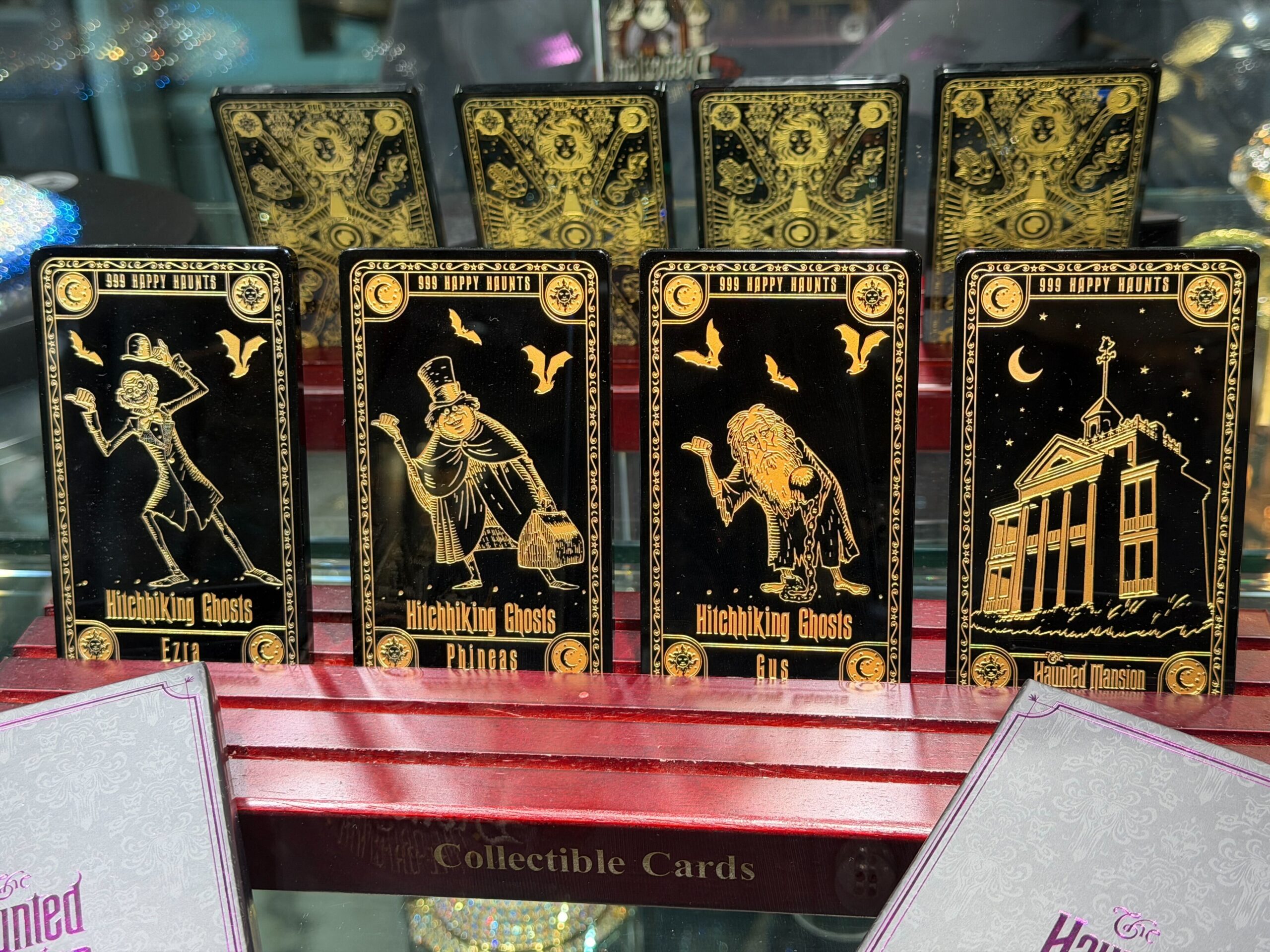 Phineas, Ezra, Gus, and the mansion are featured on the black cards with gold details. "999 Happy Haunts" text is featured on the top, and "Hitchhiking Ghosts" text is on the bottom. Each card also has the name of the ghost.