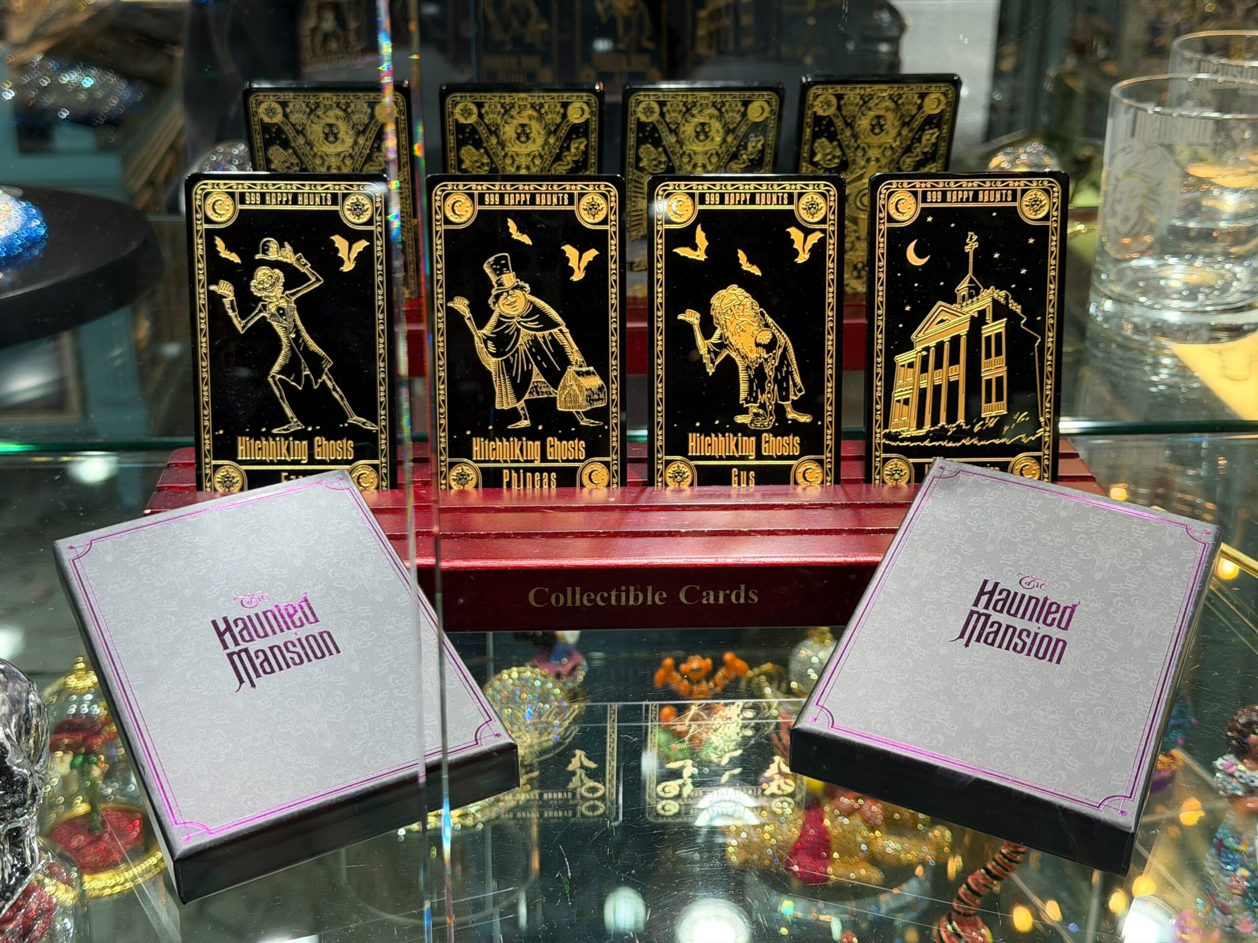 Phineas, Ezra, Gus, and the mansion are featured on the black cards with gold details. "999 Happy Haunts" text is featured on the top, and "Hitchhiking Ghosts" text is on the bottom. Each card also has the name of the ghost.
