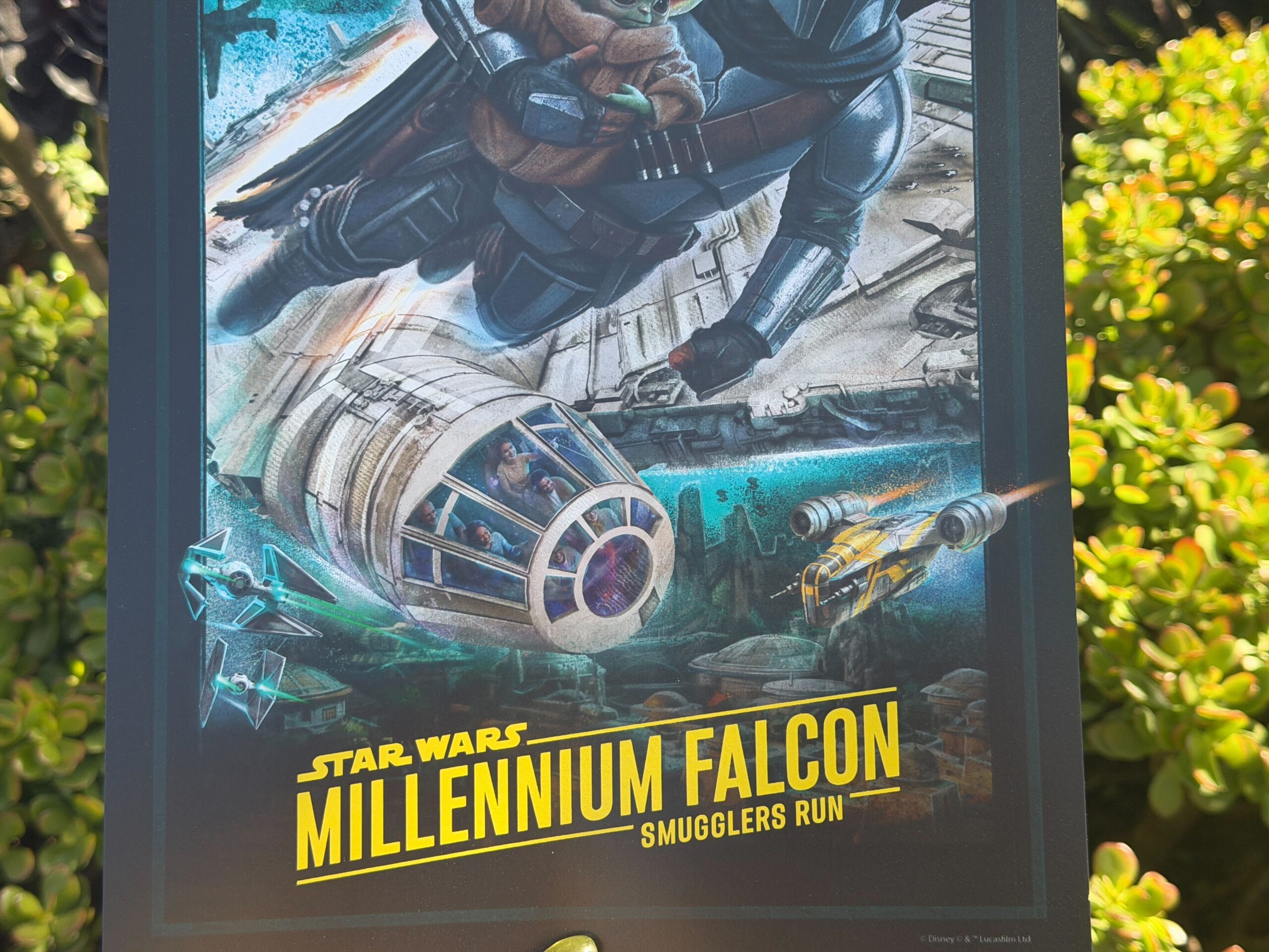The attraction poster is reminiscent of the first concept art Disney shared but viewed from outside the Millennium Falcon rather than inside. Mando holds Grogu as he flies alongside the ship above Batuu. A TIE Fighter and a yellow ST-70 assault ship similar to Mando’s old Razor Crest fly nearby. In the sky above are the ruins of the Death Star, an Imperial shuttle, and an Imperial landing craft.